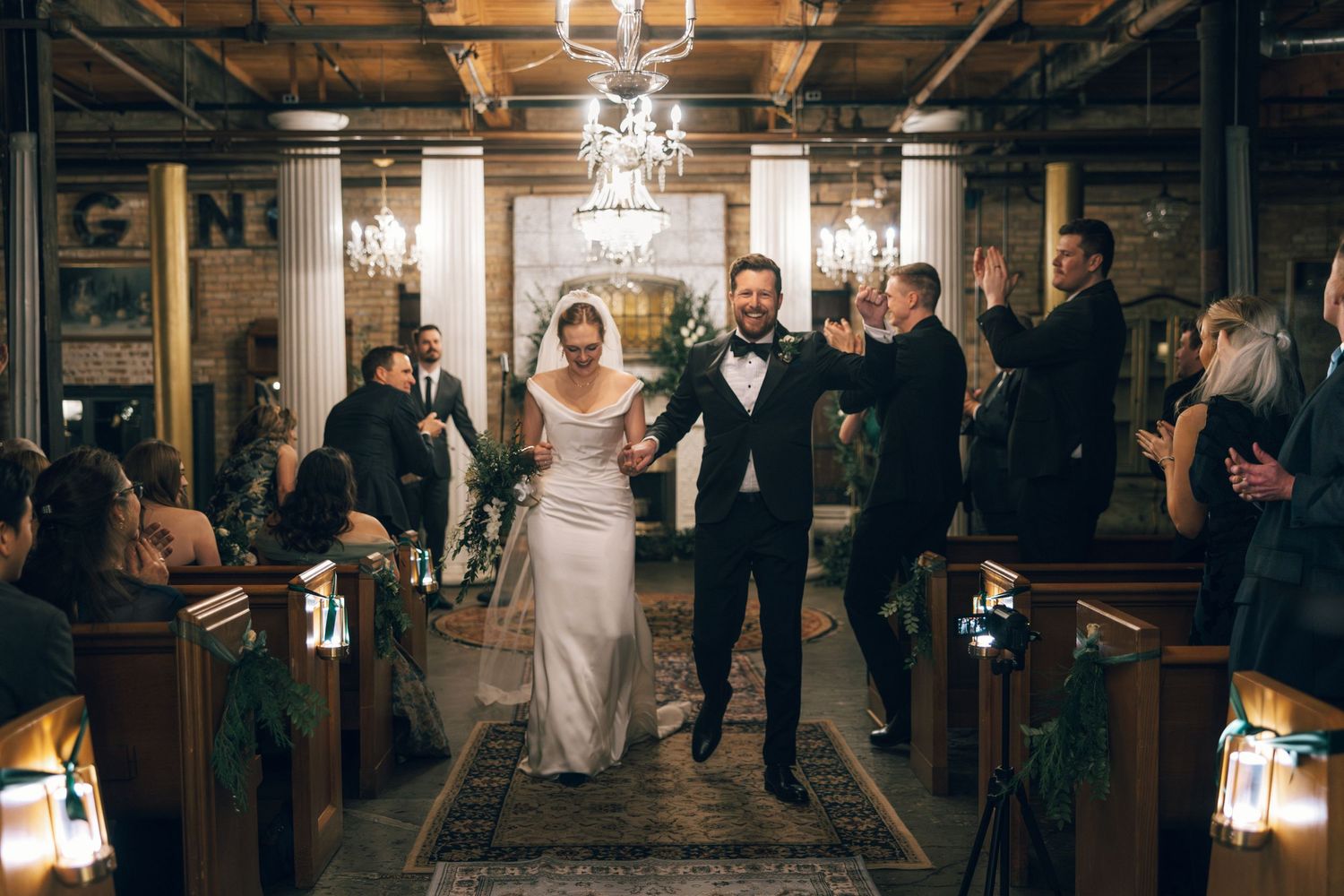 A bride and groom share their first dance under crystal chandeliers in an elegant ballroom surrounded by guests.