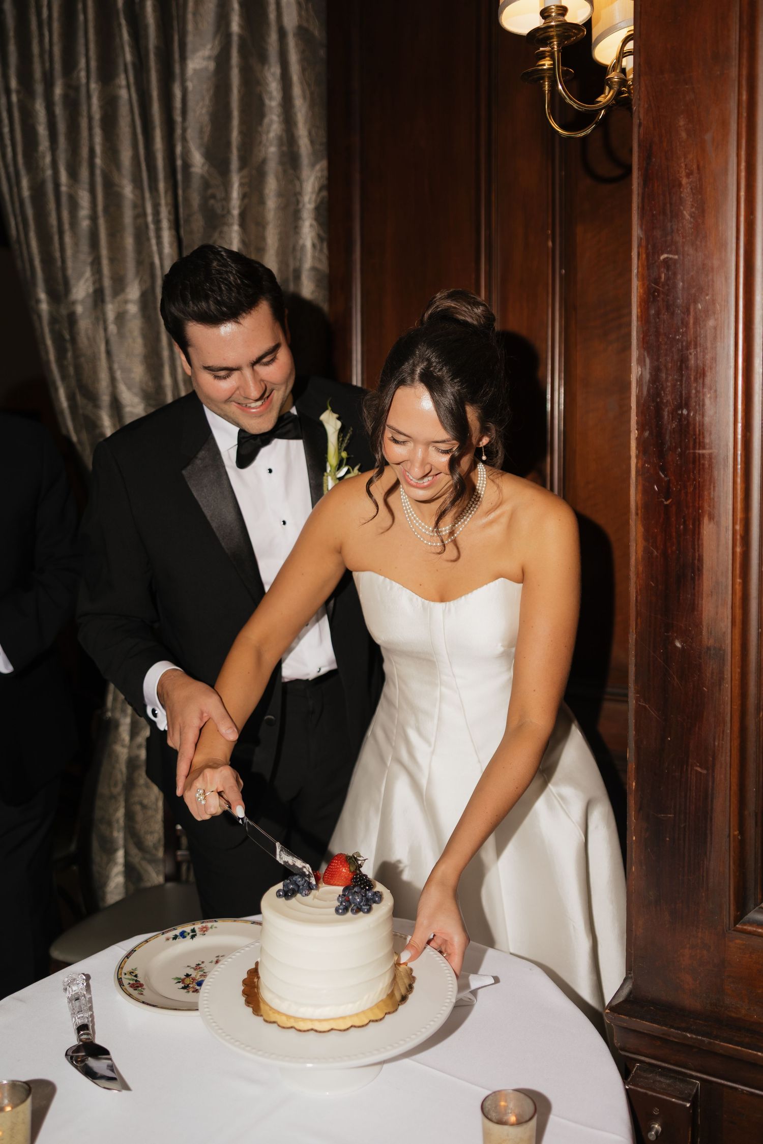 Bride and groom cutting white wedding cake with fresh berries at elegant reception venue.