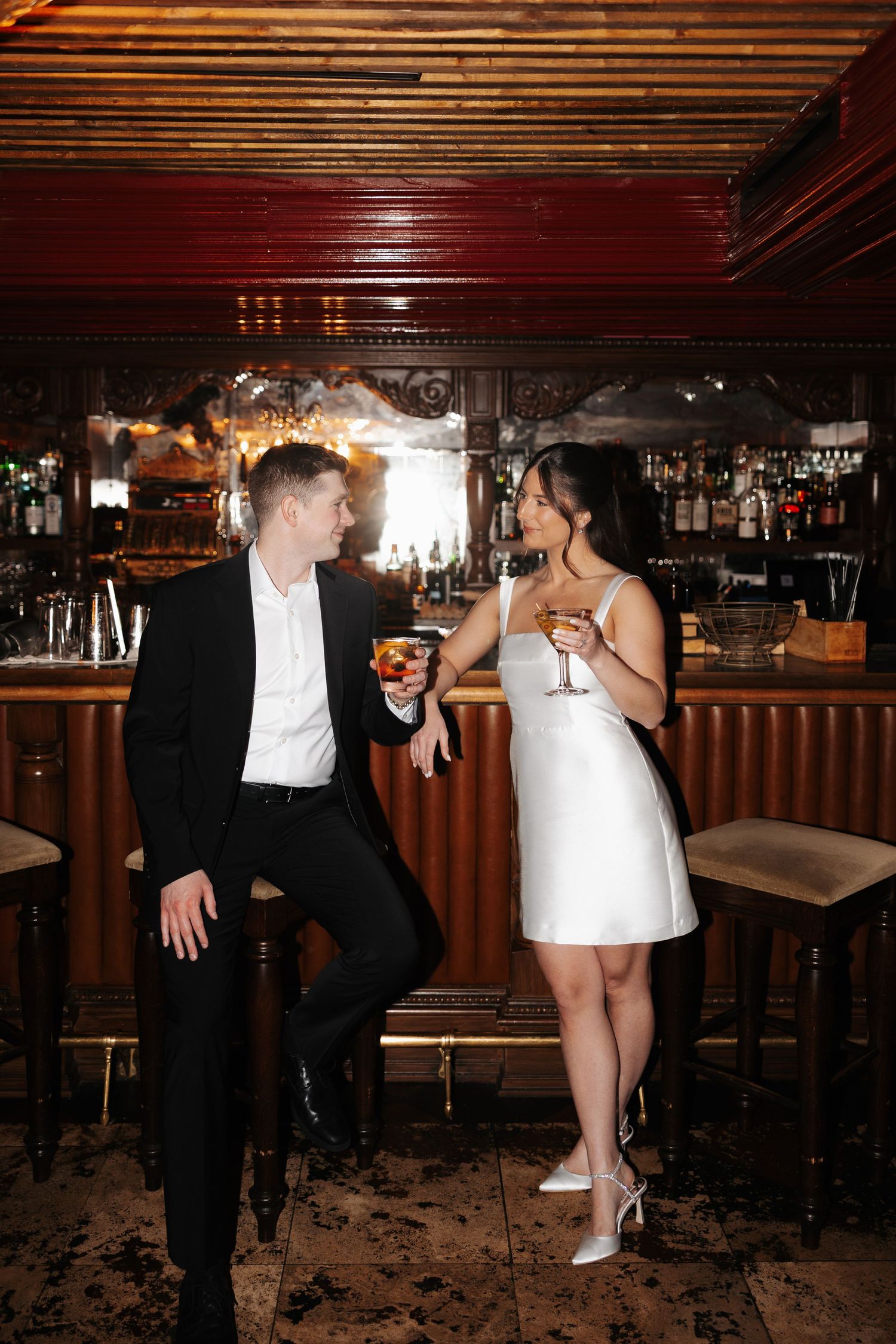 A couple in formal attire shares a playful dance moment at the bar during a celebration.