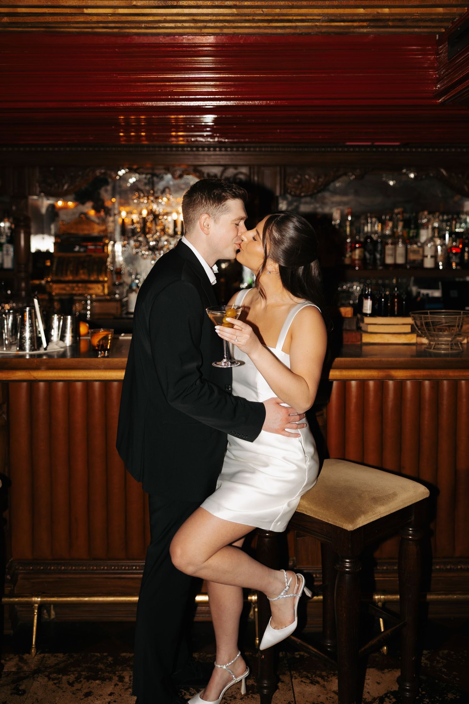A romantic moment between a couple in formal attire sharing a passionate kiss at a dimly lit venue.