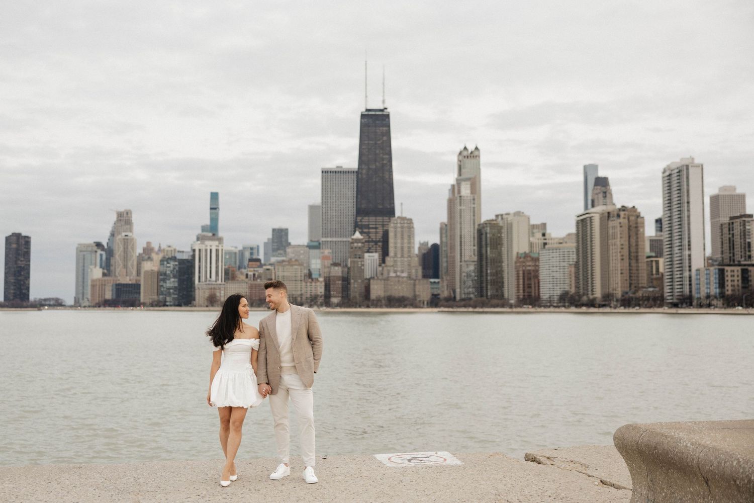 Romantic couple gazing at each other on Chicago waterfront with John Hancock Tower visible.