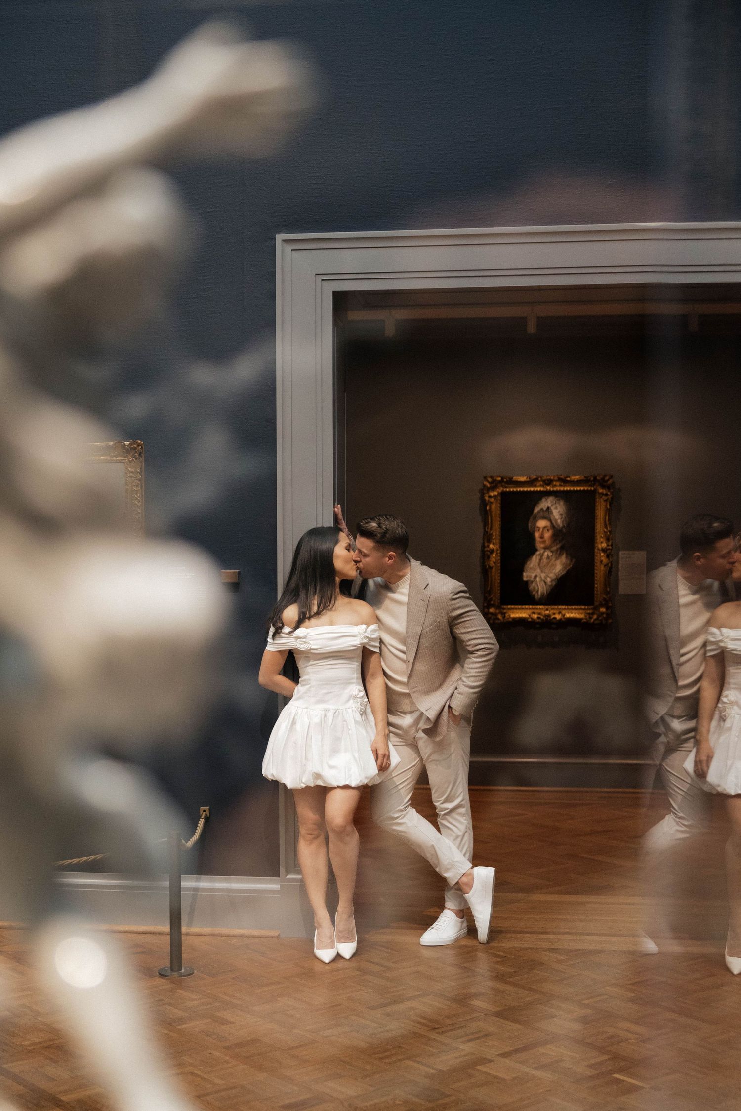 Couple sharing a romantic moment in an art museum gallery with classical paintings and sculptures.