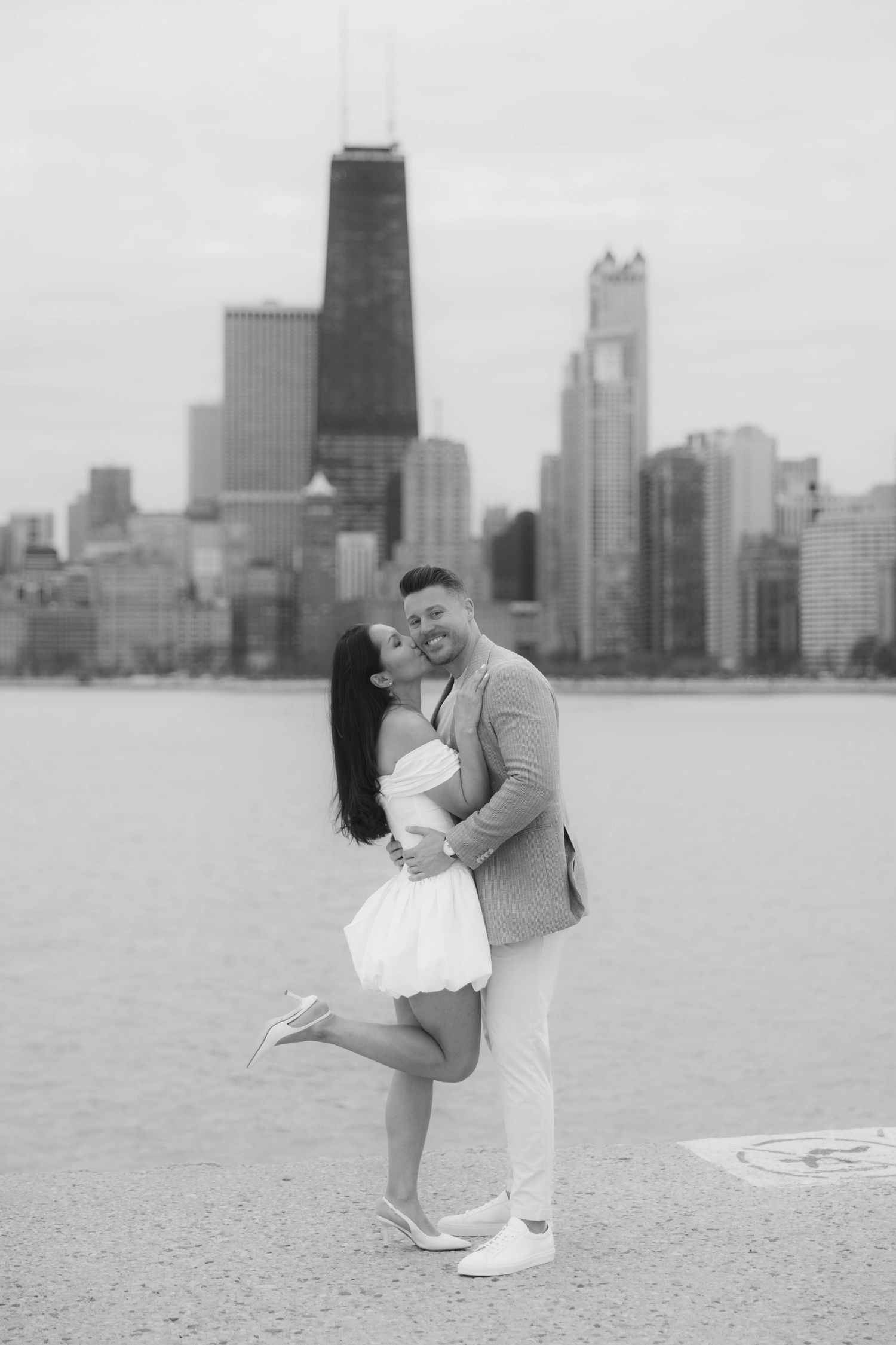 Black and white engagement photo of couple embracing with Chicago skyline behind them.
