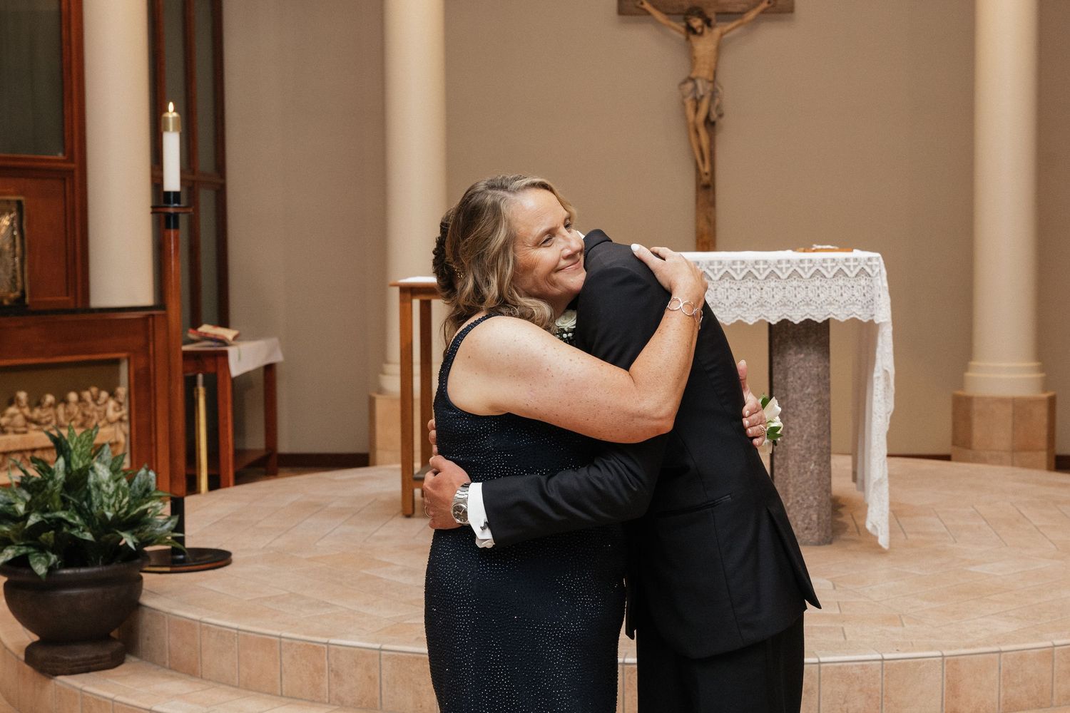 A couple shares a warm embrace near the altar of a church, with a crucifix visible on the wall behind them.