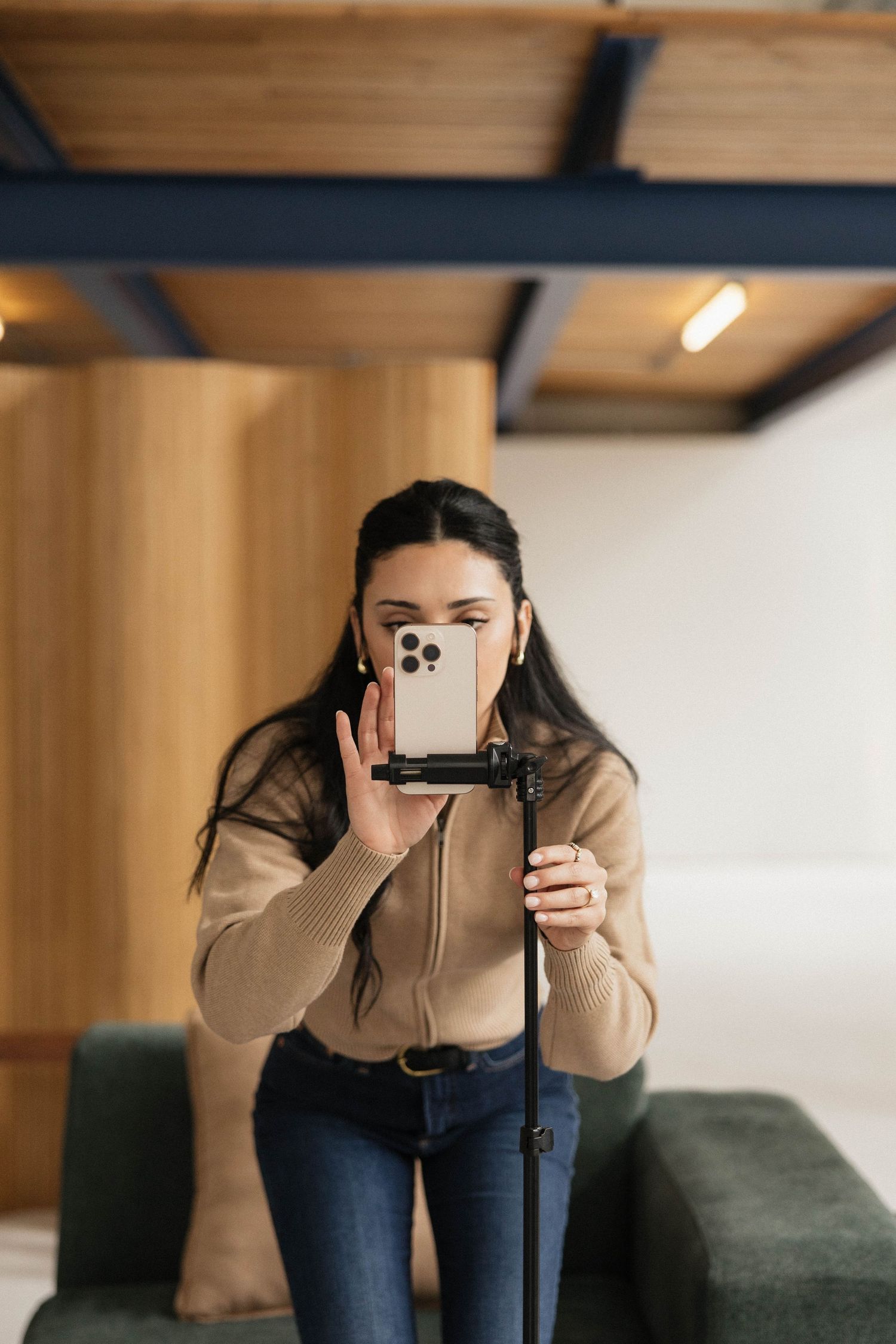 Young woman setting up smartphone on tripod stand for video recording in modern interior space.