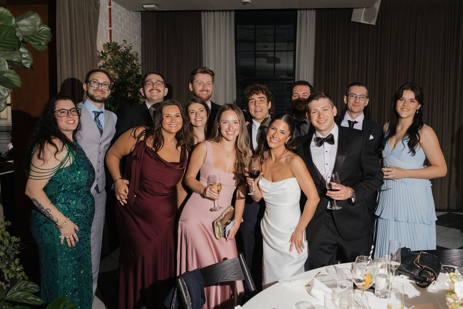 Group of elegantly dressed wedding guests smiling together at a formal reception venue.