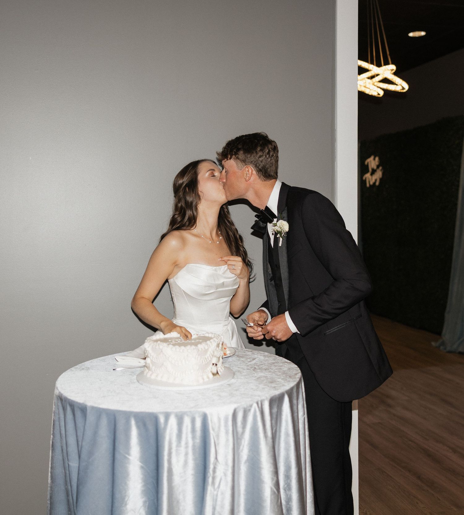 Bride and groom sharing a kiss while cutting their white wedding cake at their elegant indoor reception.