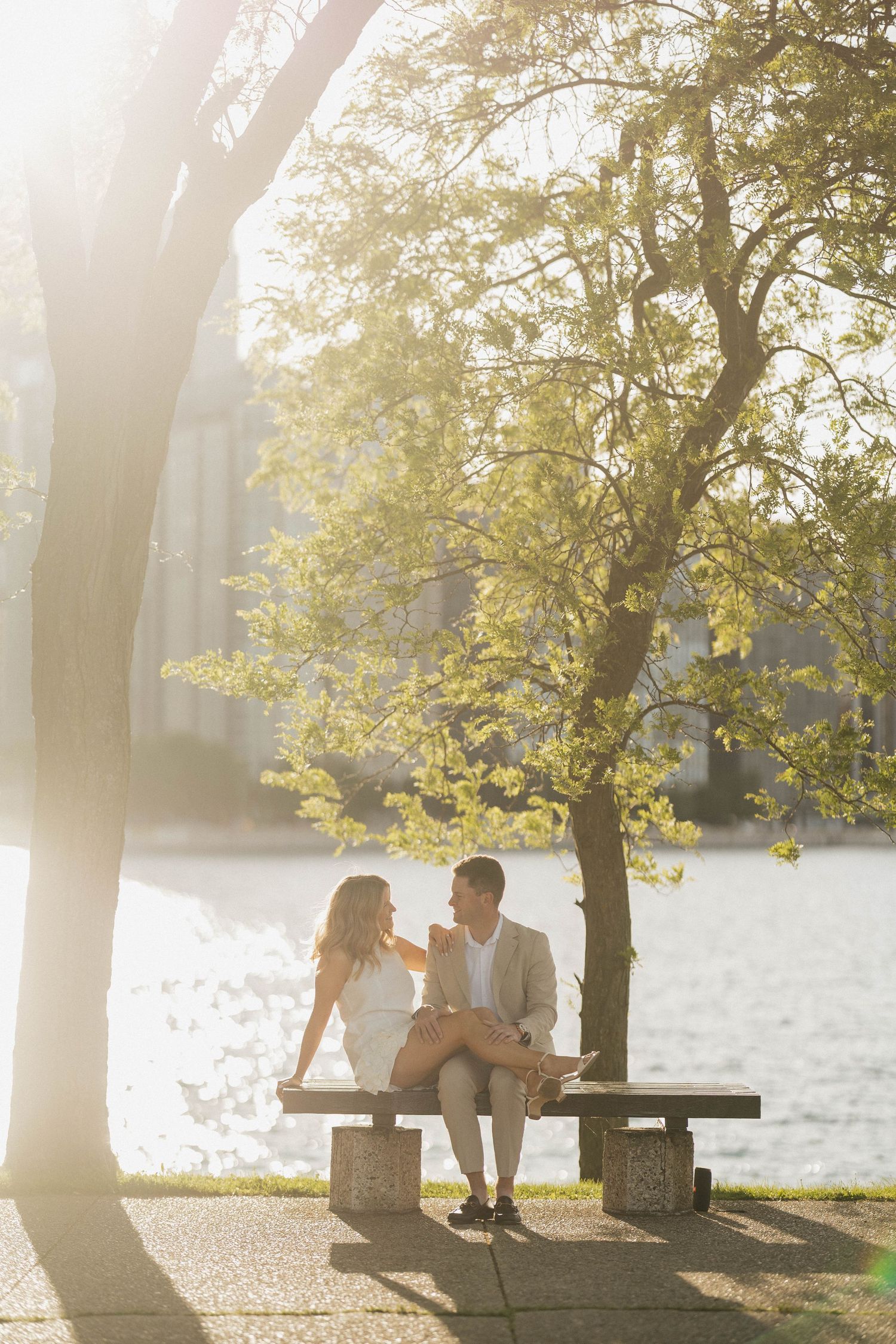 Couple sitting on a bench by the waterfront under golden sunlight, sharing a romantic moment.