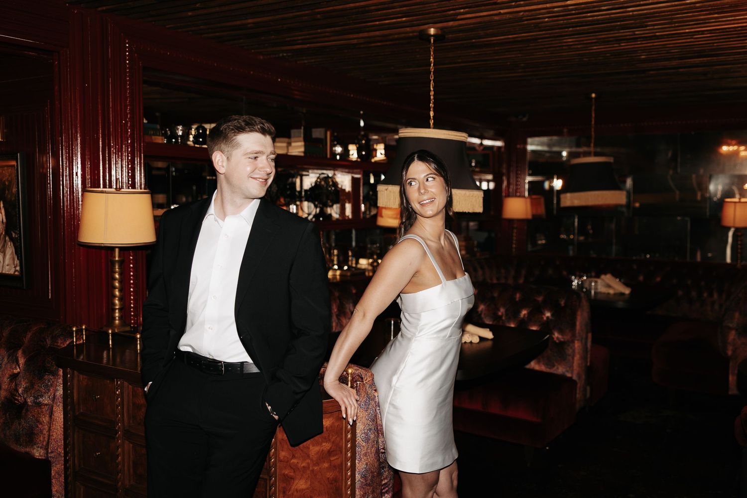 A couple dances together in an elegant ballroom setting with warm lighting and dark wood decor.
