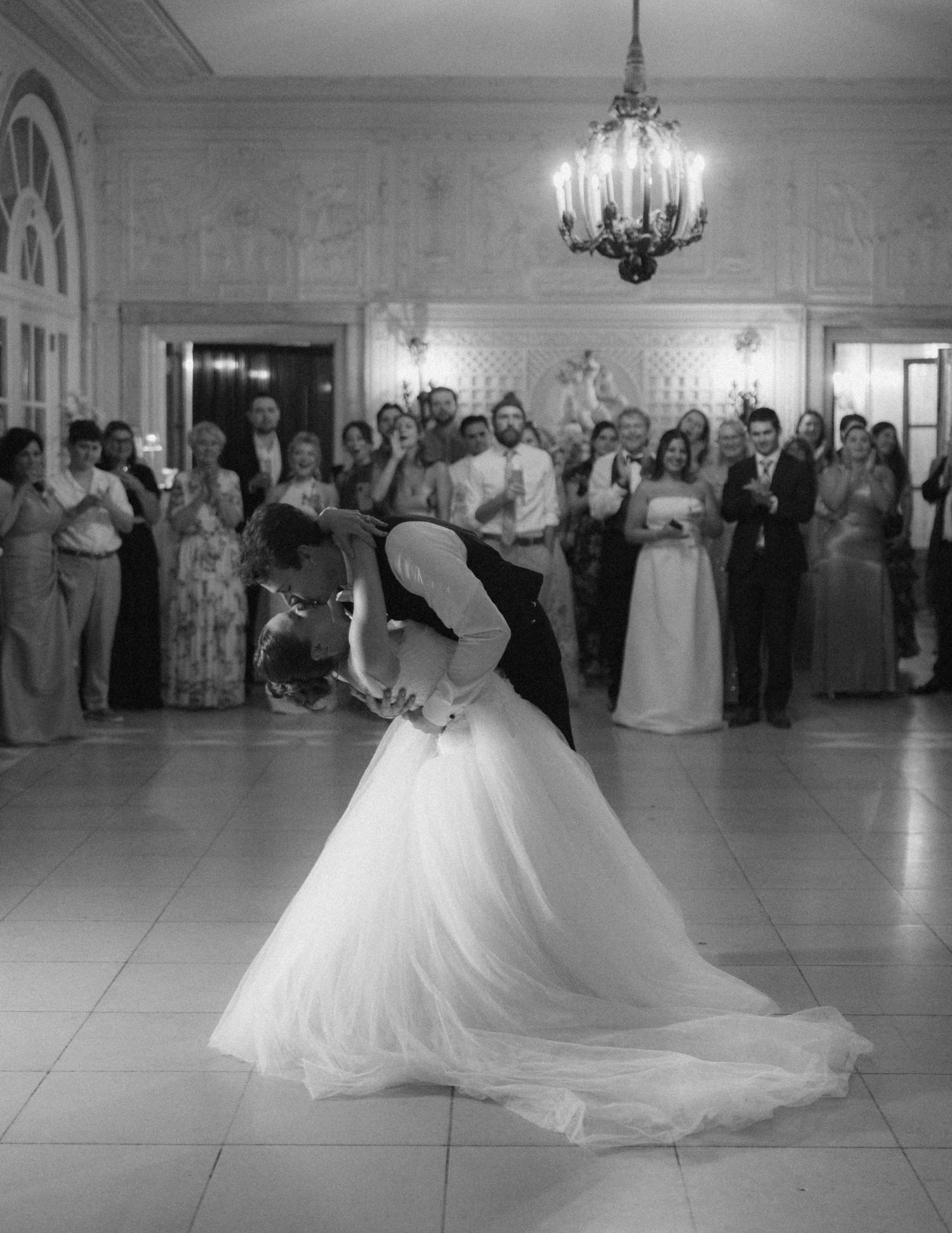 Black and white photo of a bride and groom sharing their first dance dip at an elegant wedding reception.