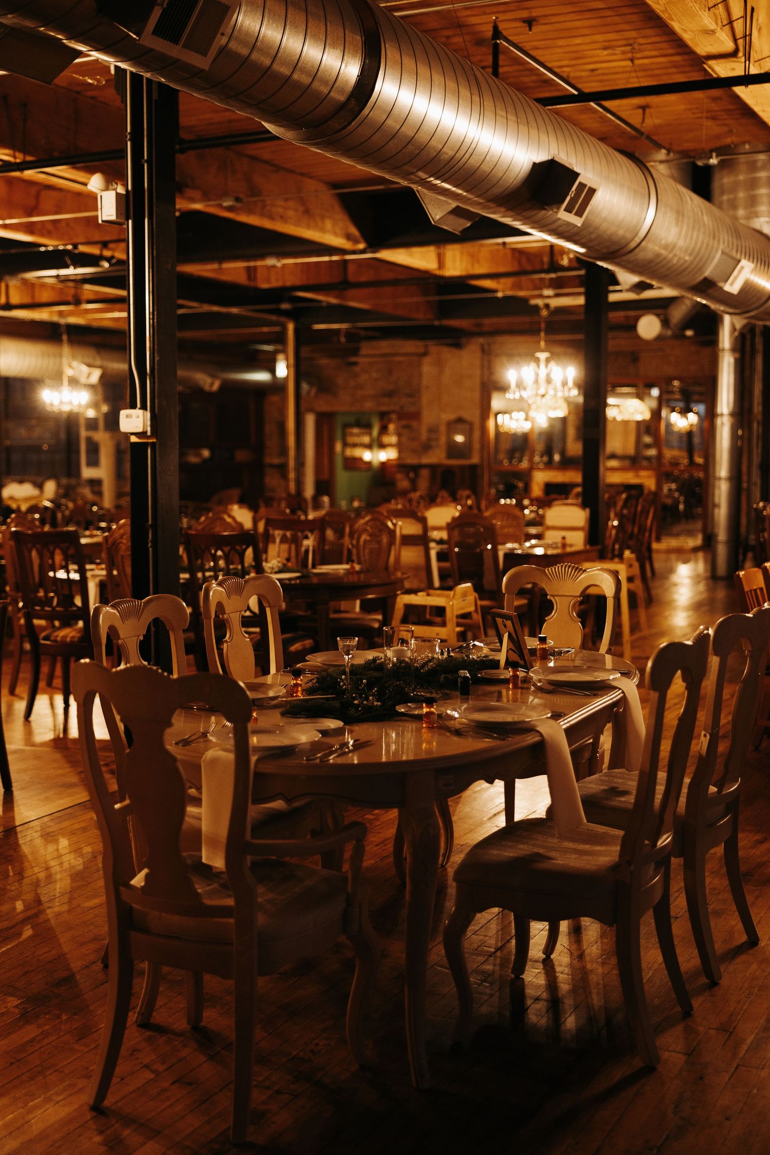 Rustic restaurant interior with exposed ductwork, wooden chairs, and warm lighting creates an intimate industrial atmosphere.