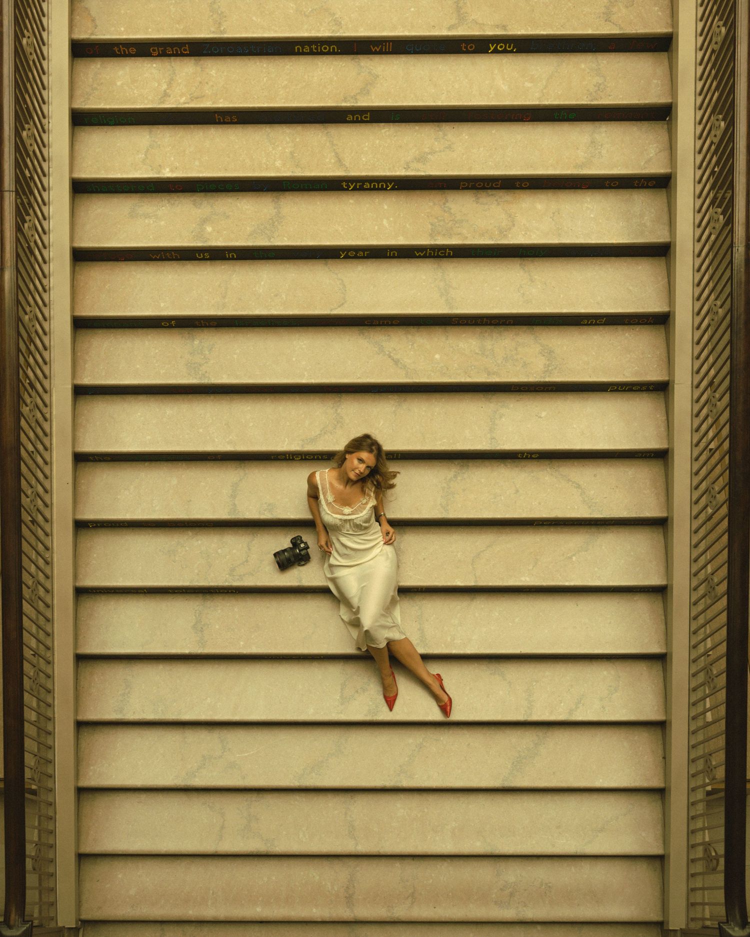 Woman in white dress lying on marble steps with a camera beside her, viewed from above.