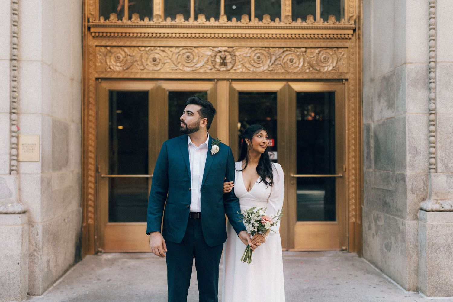 A bride and groom share an intimate moment in front of an ornate stone building with wooden doors.