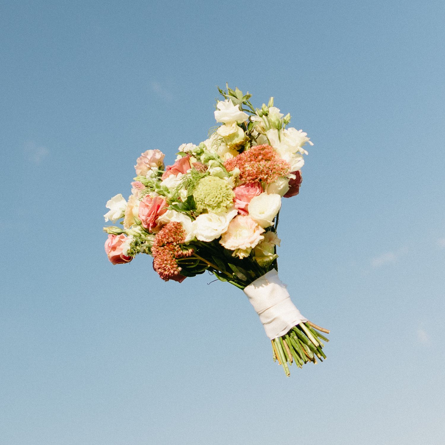 Wedding bouquet with coral and cream flowers tossed against a blue sky.