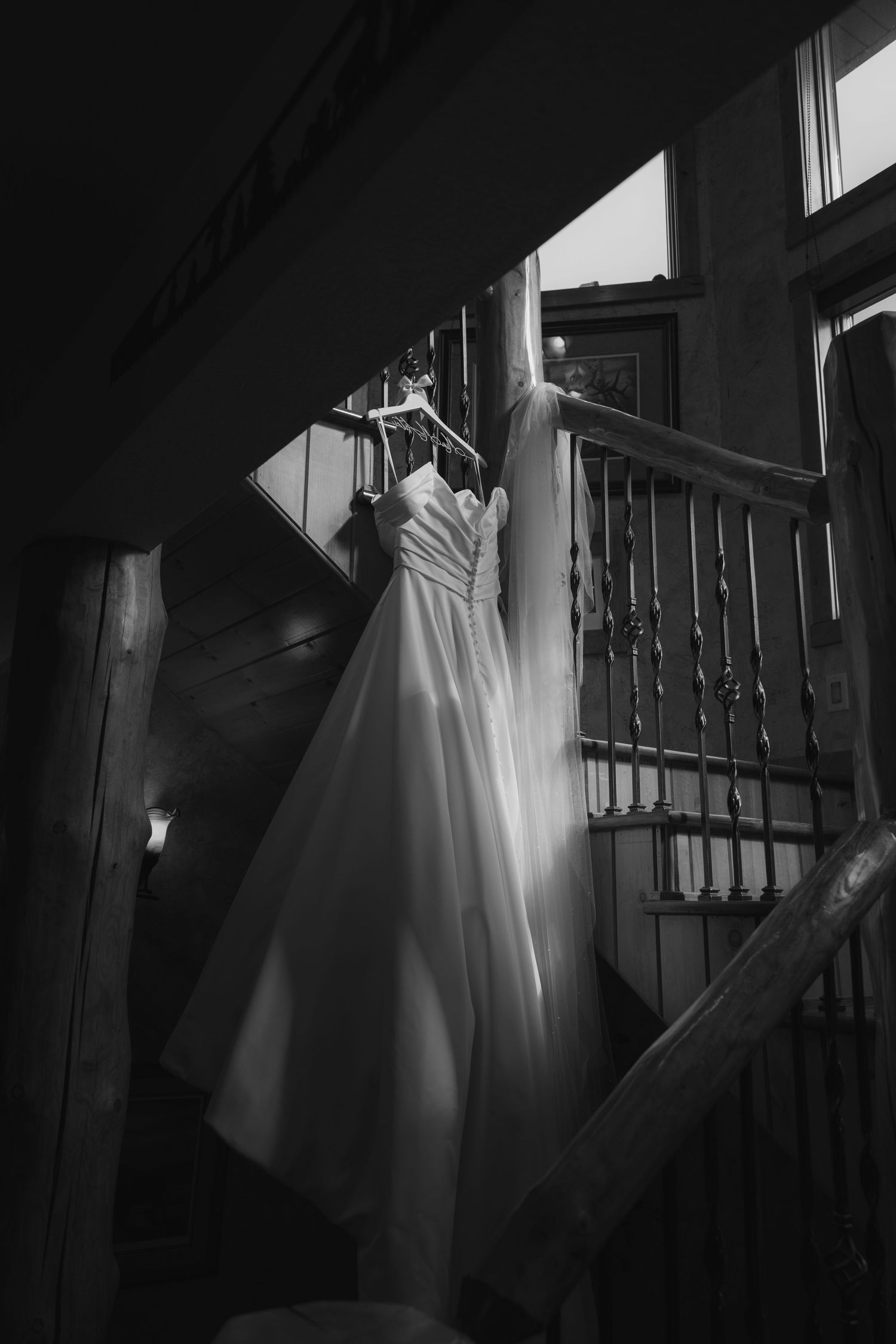 Wedding dress hanging in dramatic lighting against dark staircase railing.