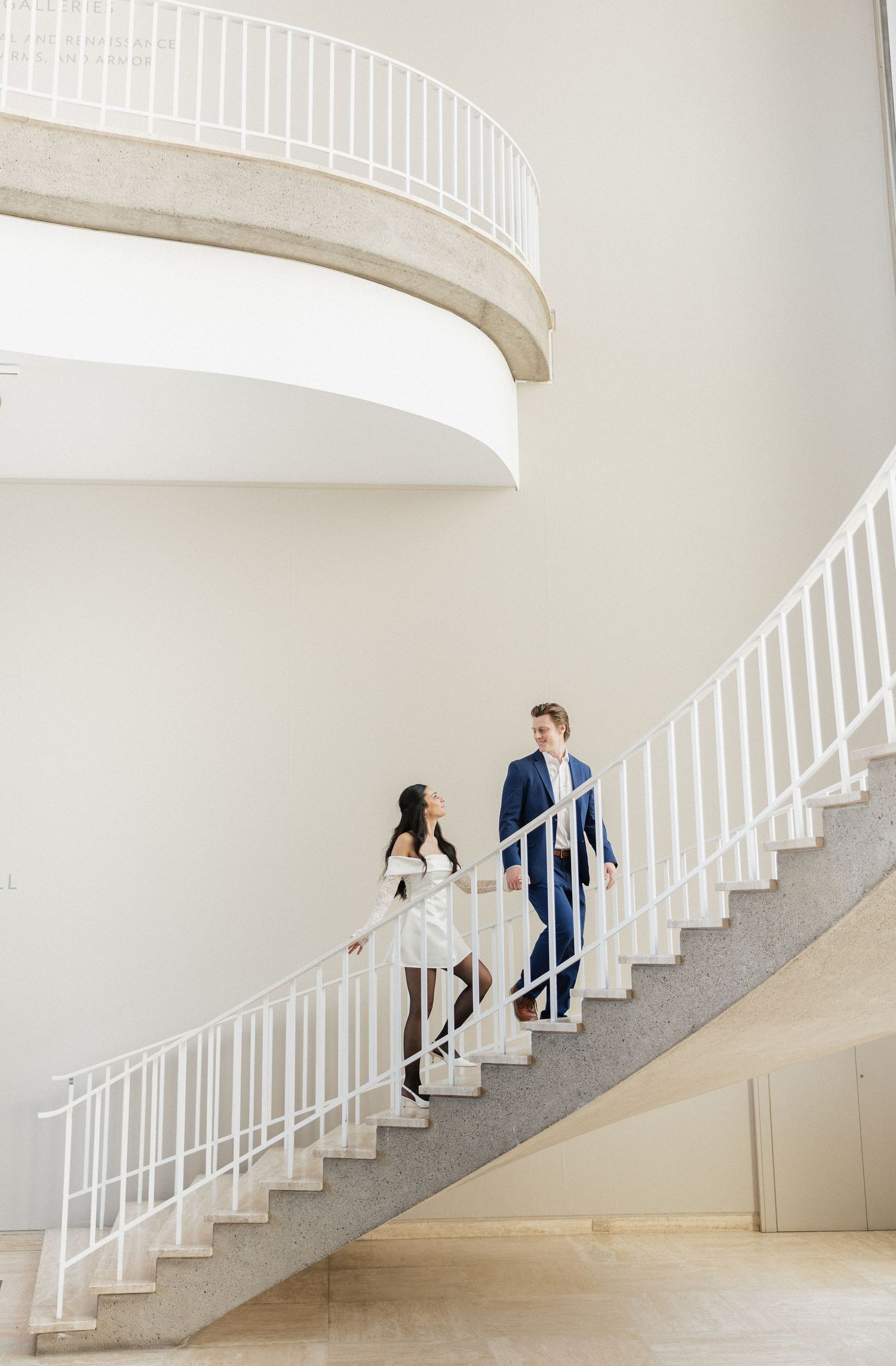 Elegant white spiral staircase photos showing people ascending and descending in formal attire.