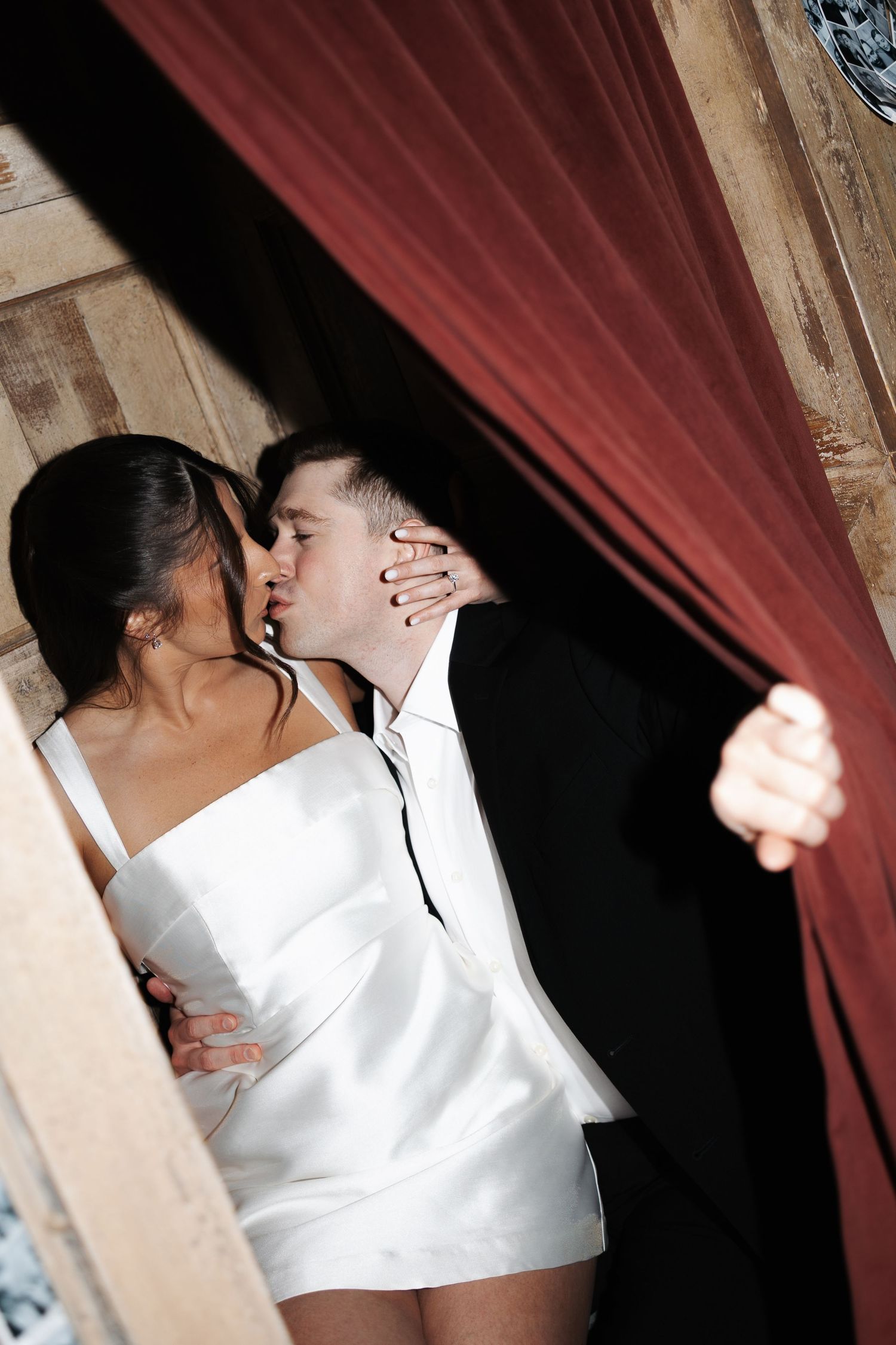A couple dancing closely together in front of a red curtain with dramatic lighting.