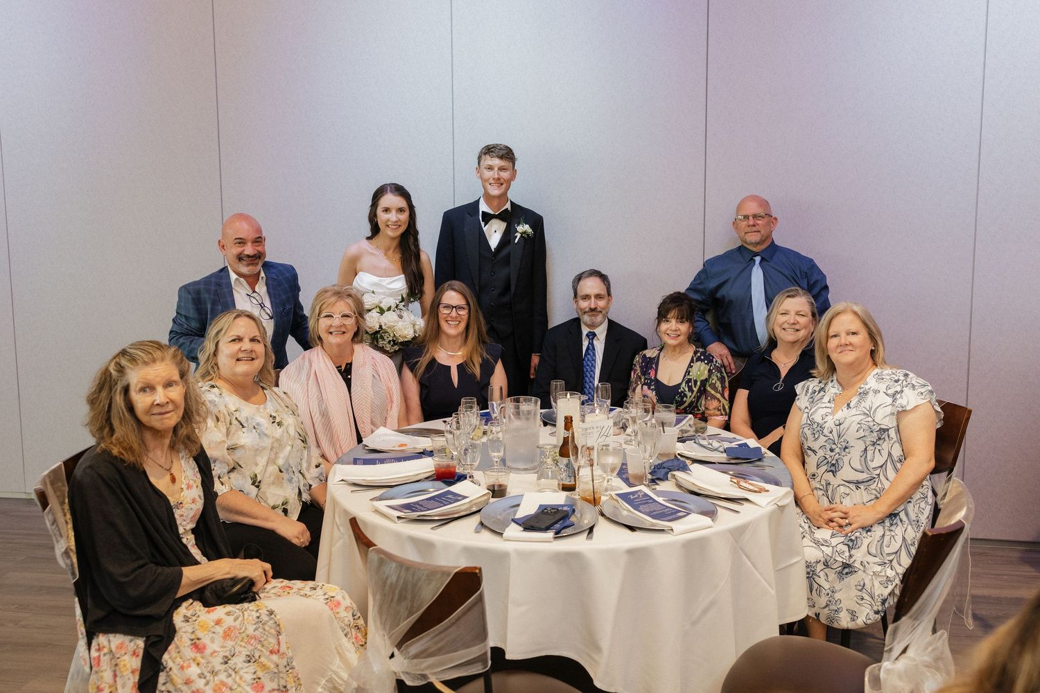 Wedding reception group photo with bride and groom surrounded by family at an elegantly set round dining table.