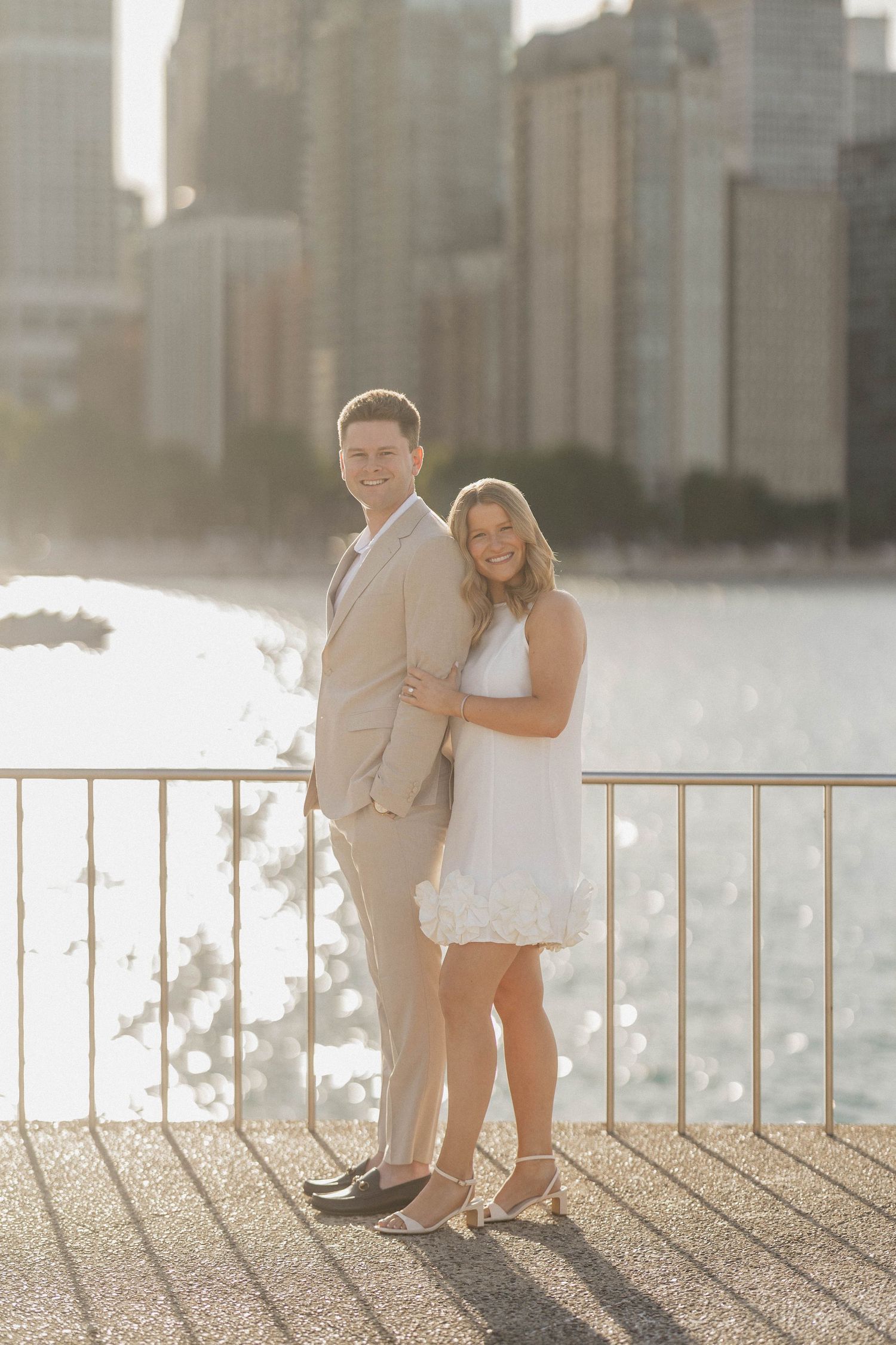 Couple poses together on waterfront promenade with golden sunlit Chicago skyline in background.