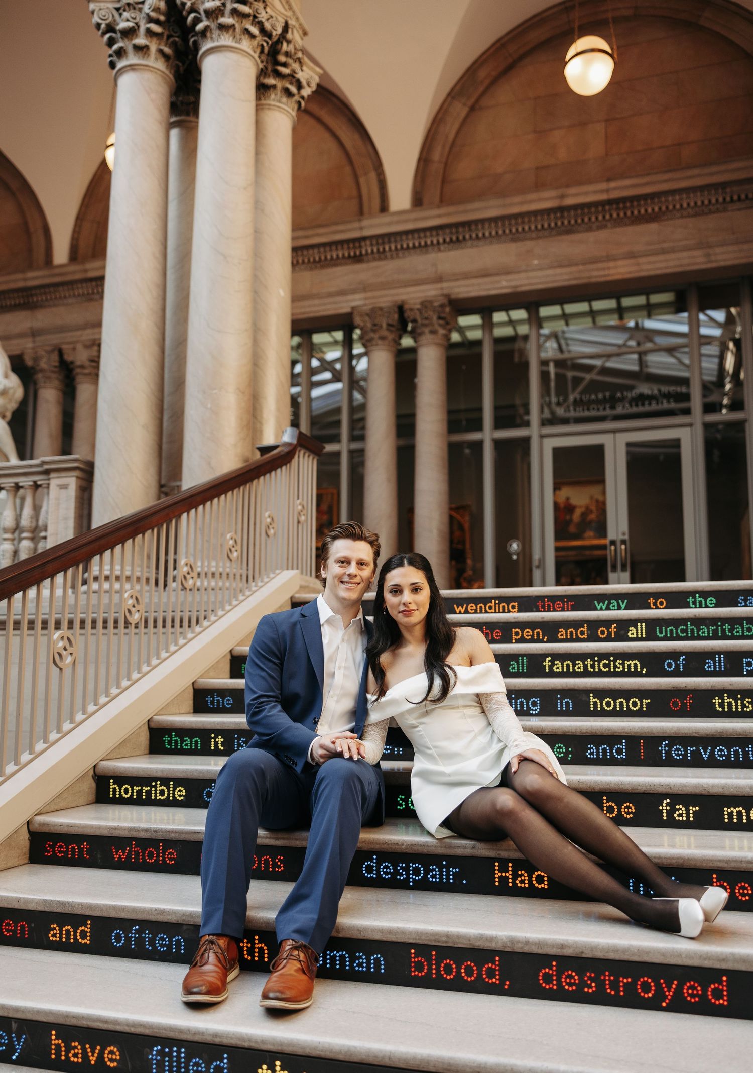 A couple sits together on historic marble steps with text displays.