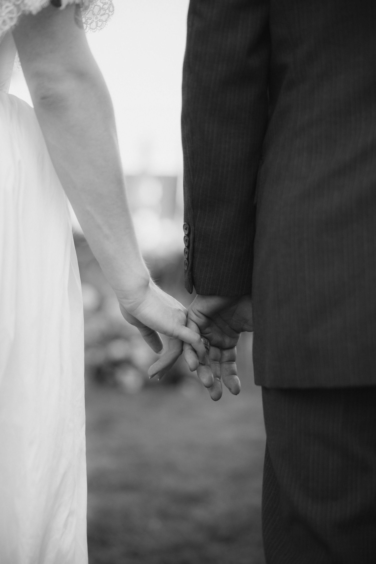 Black and white photo of bride and groom holding hands, wedding couple closeup showing elegant dress and suit.