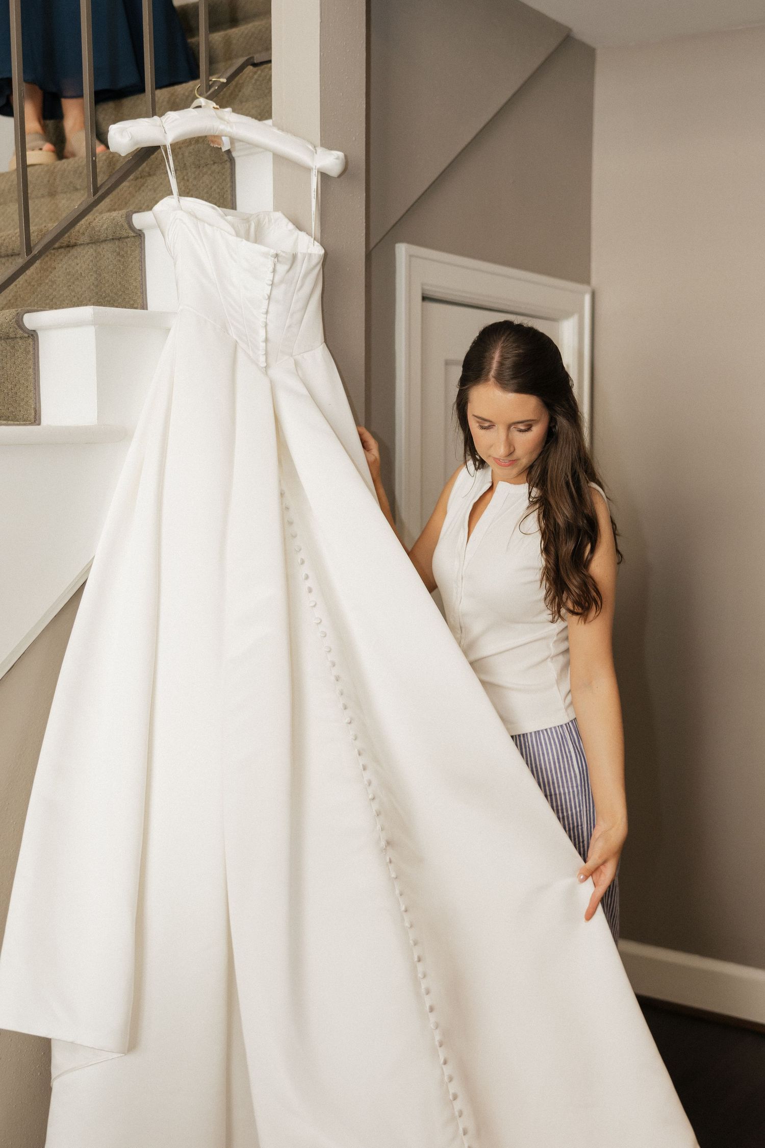 Bride admiring her elegant white wedding dress hanging on a staircase banister before her ceremony.