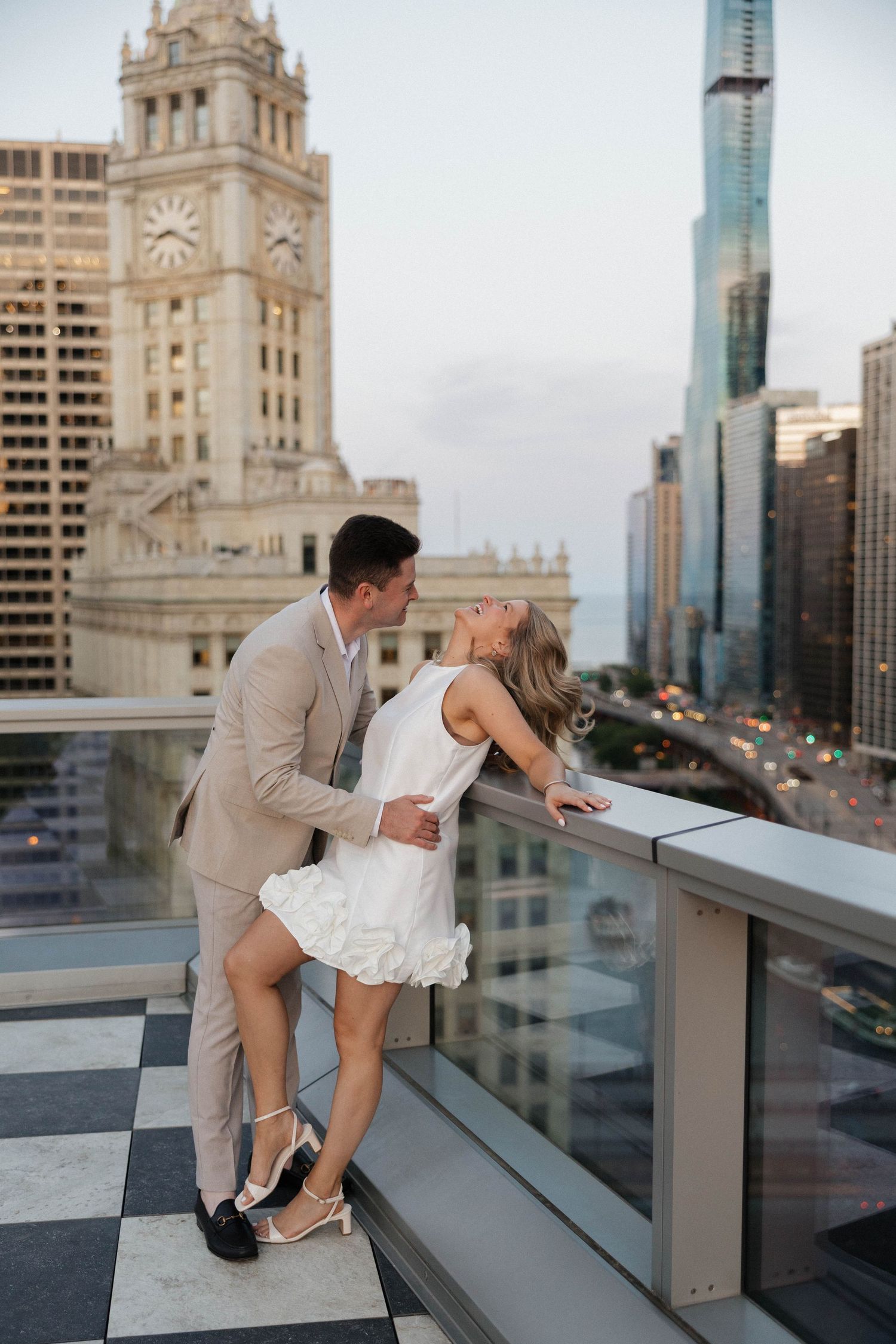 Couple shares a kiss on rooftop terrace with iconic Chicago Wrigley Building and skyline at dusk.