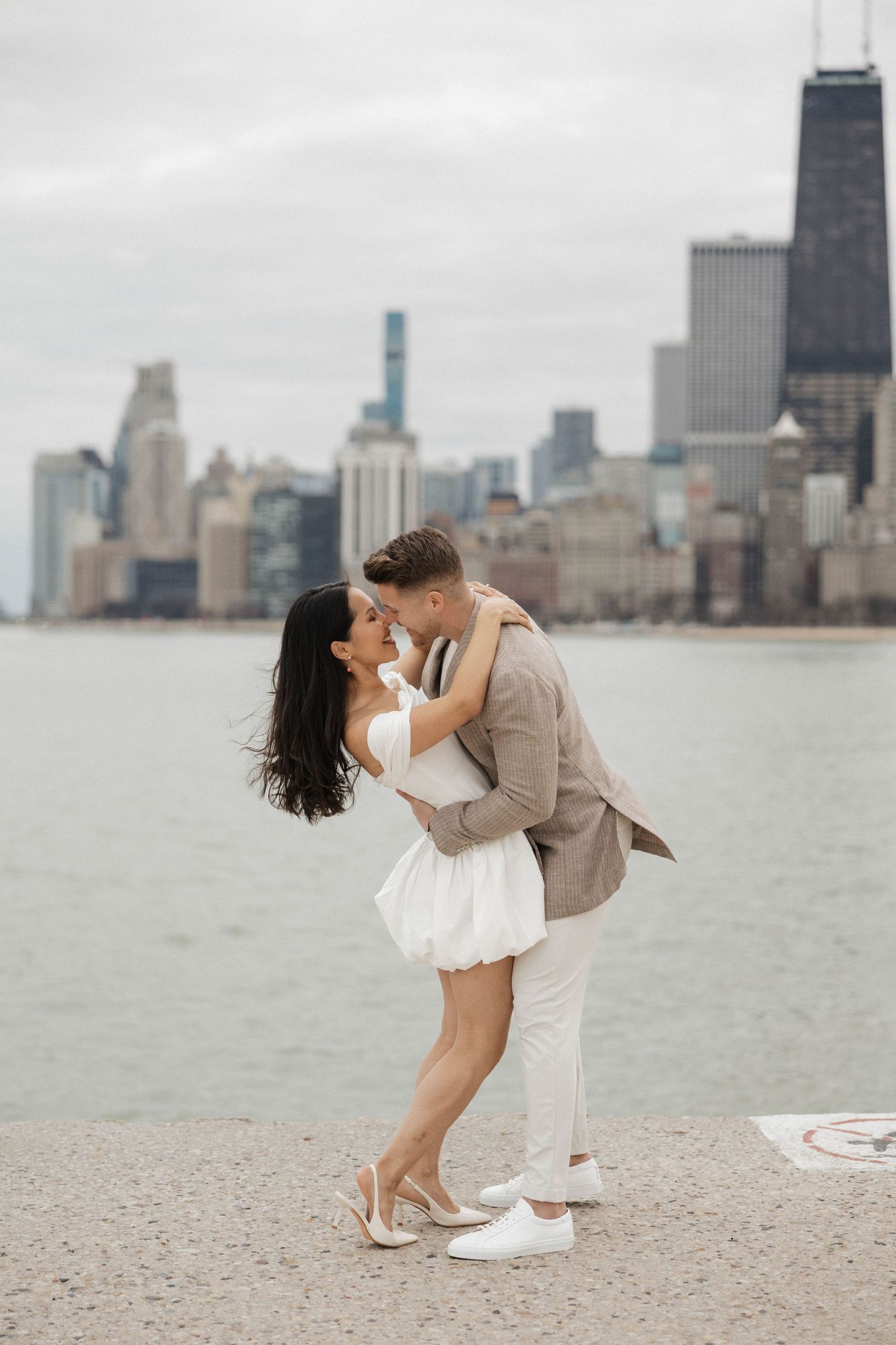 Couple sharing a romantic dip kiss by Lake Michigan with Chicago skyline backdrop.