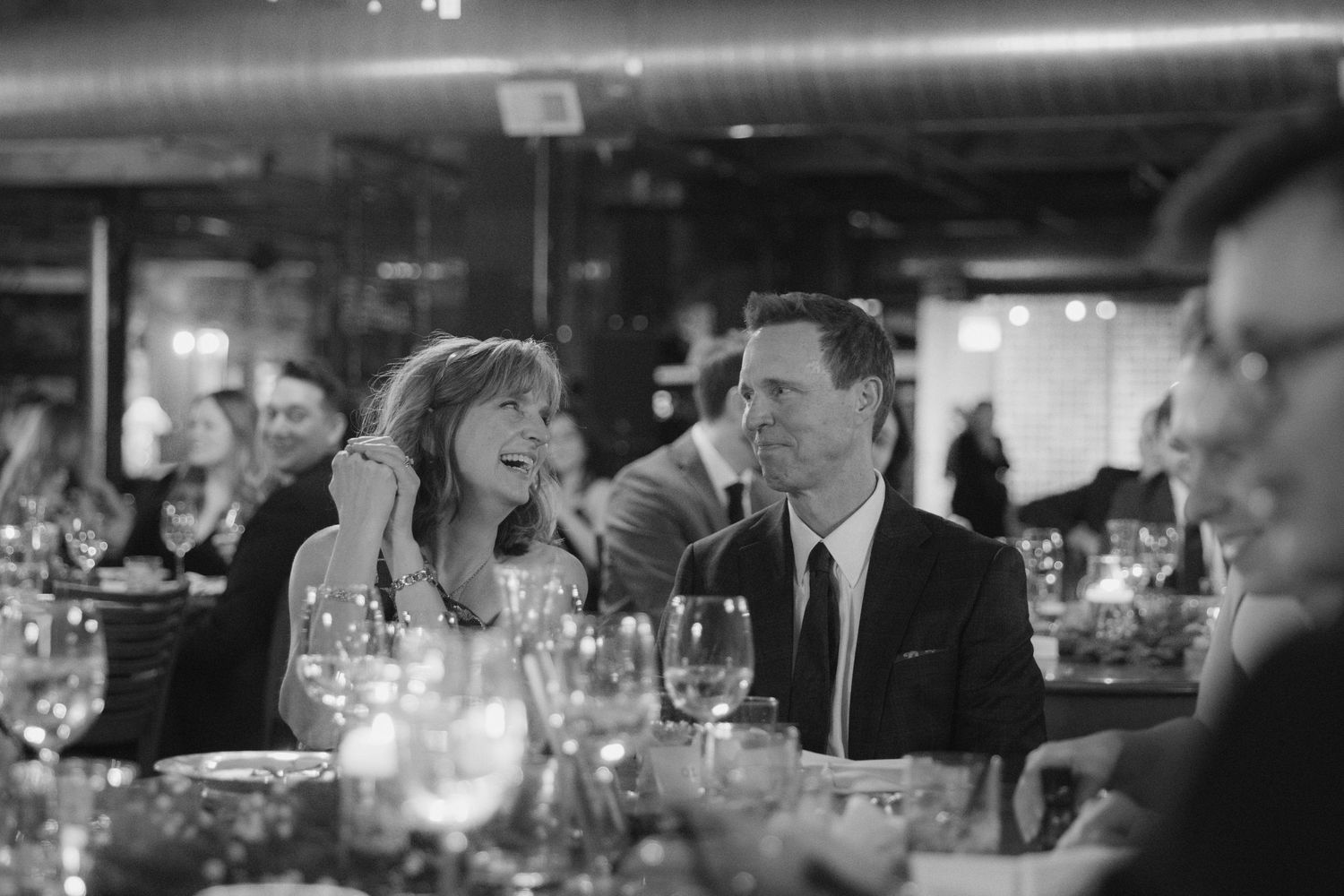 Black and white candid shots of guests enjoying conversation at an intimate indoor dinner gathering.