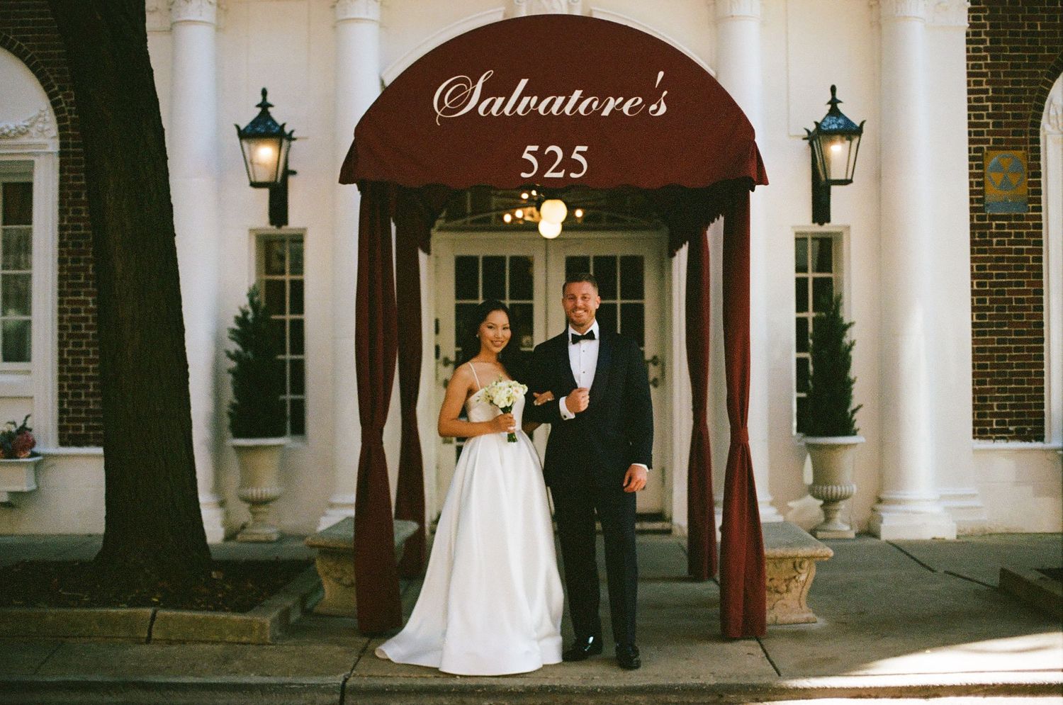 Bride and groom posing outside Salvatore's restaurant at 525, bride in white gown holding bouquet, groom in black tuxedo.