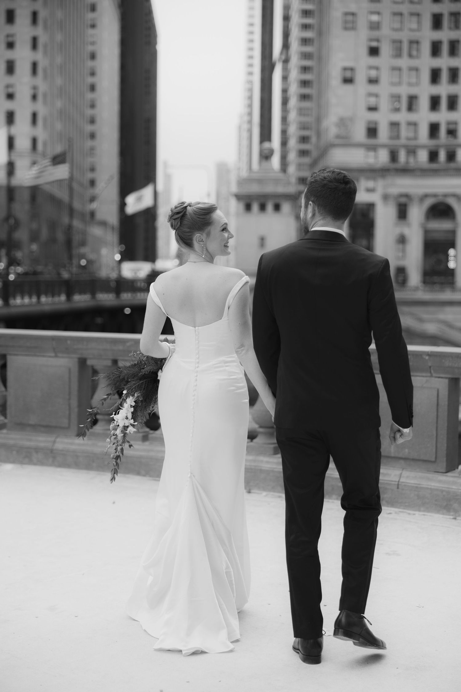 Black and white photo sequence of a bride and groom walking away together on a rooftop with city buildings in background.