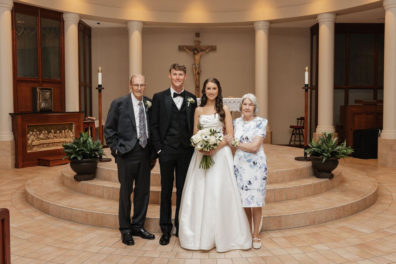 Wedding couple poses with family members at church altar, bride holding white bouquet in elegant gown.