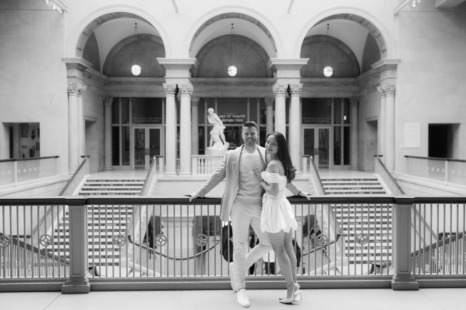 Couple posing elegantly on a balcony inside a grand museum atrium in black and white photography.