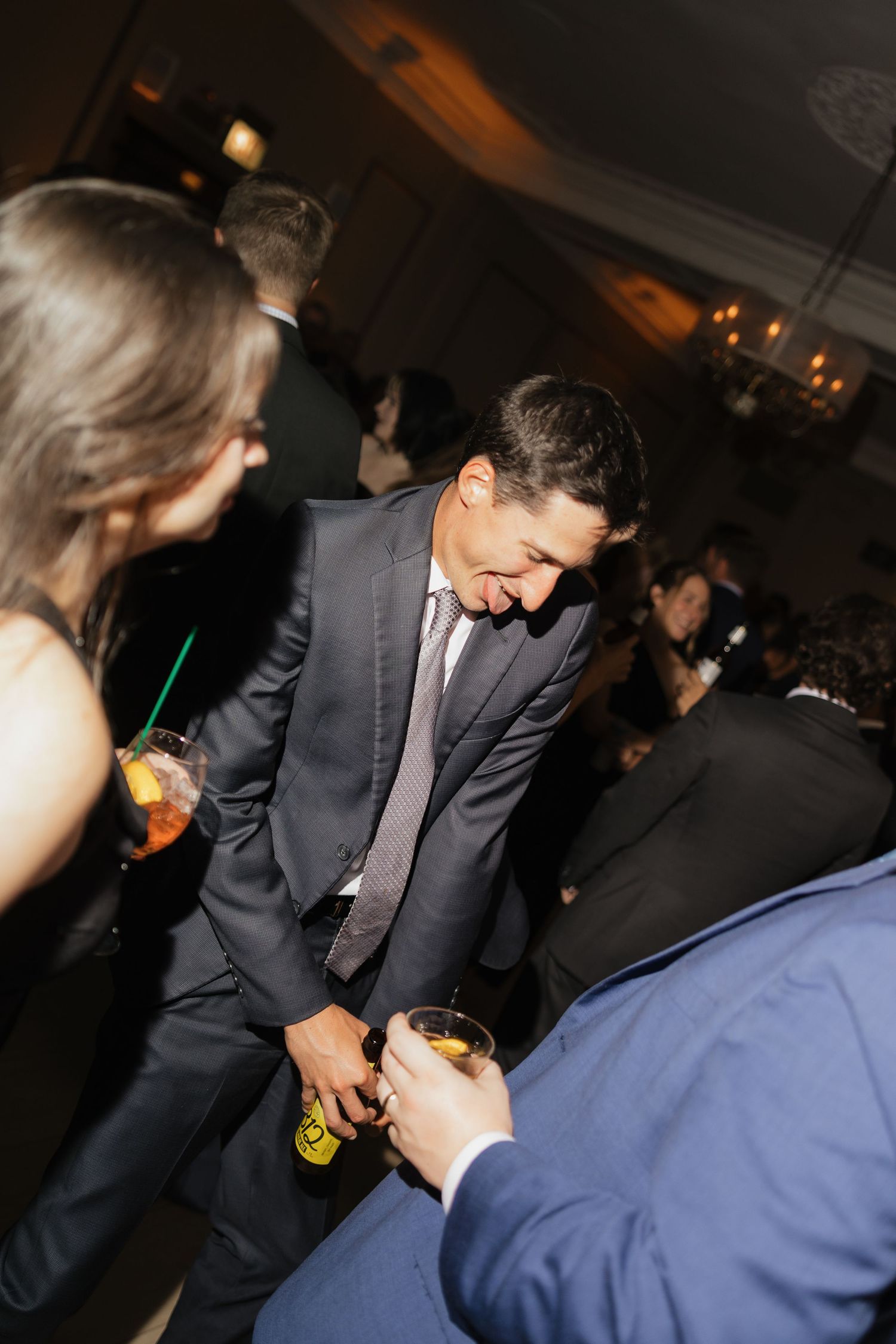 Man in dark suit and tie smiling while clinking glasses at an elegant evening social gathering.