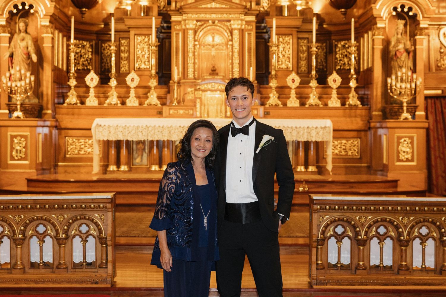 Wedding party stands in front of gilded altar in traditional church with baroque architecture.