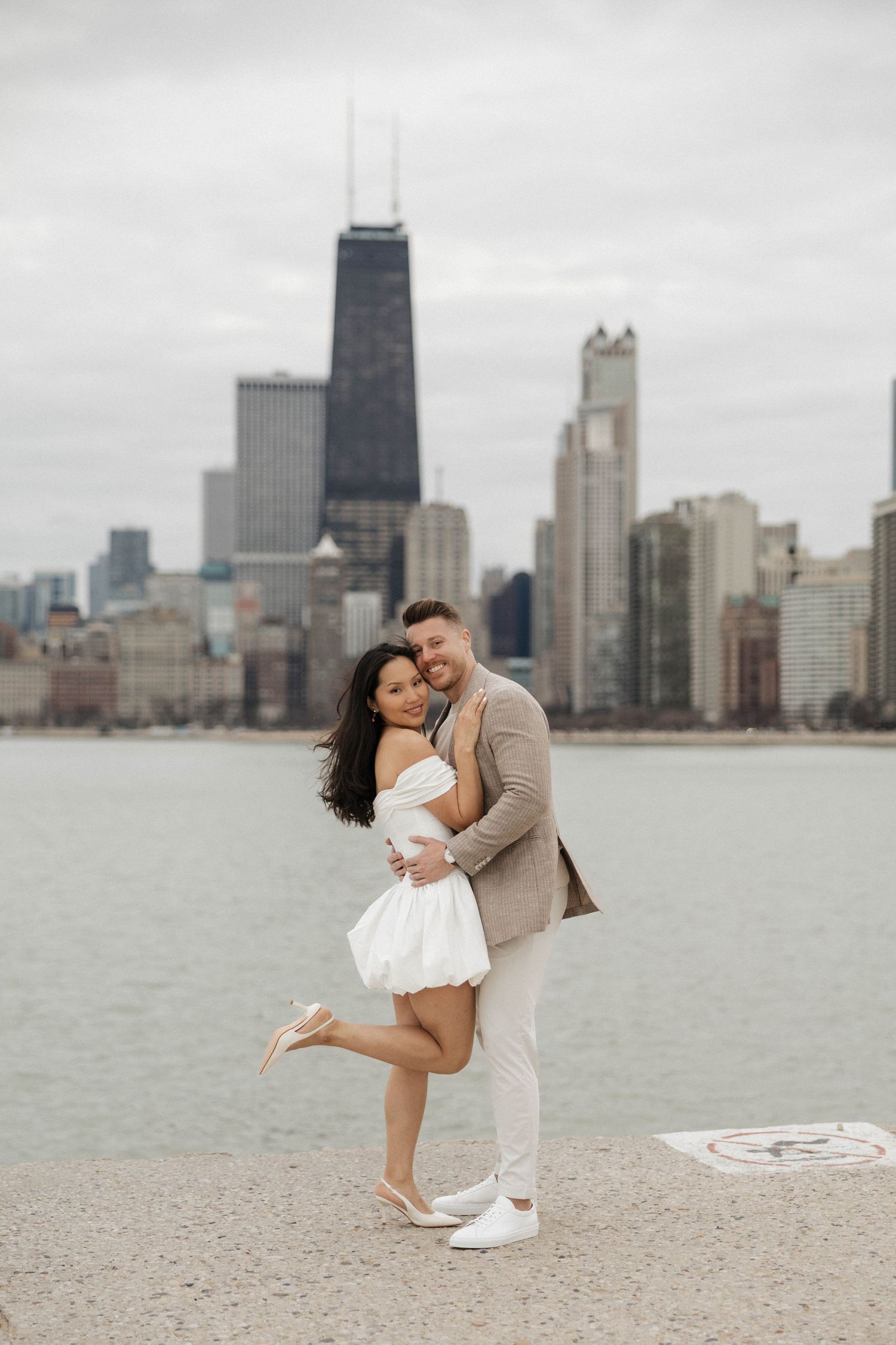 Happy couple embracing and smiling on Chicago waterfront with city skyline behind them.
