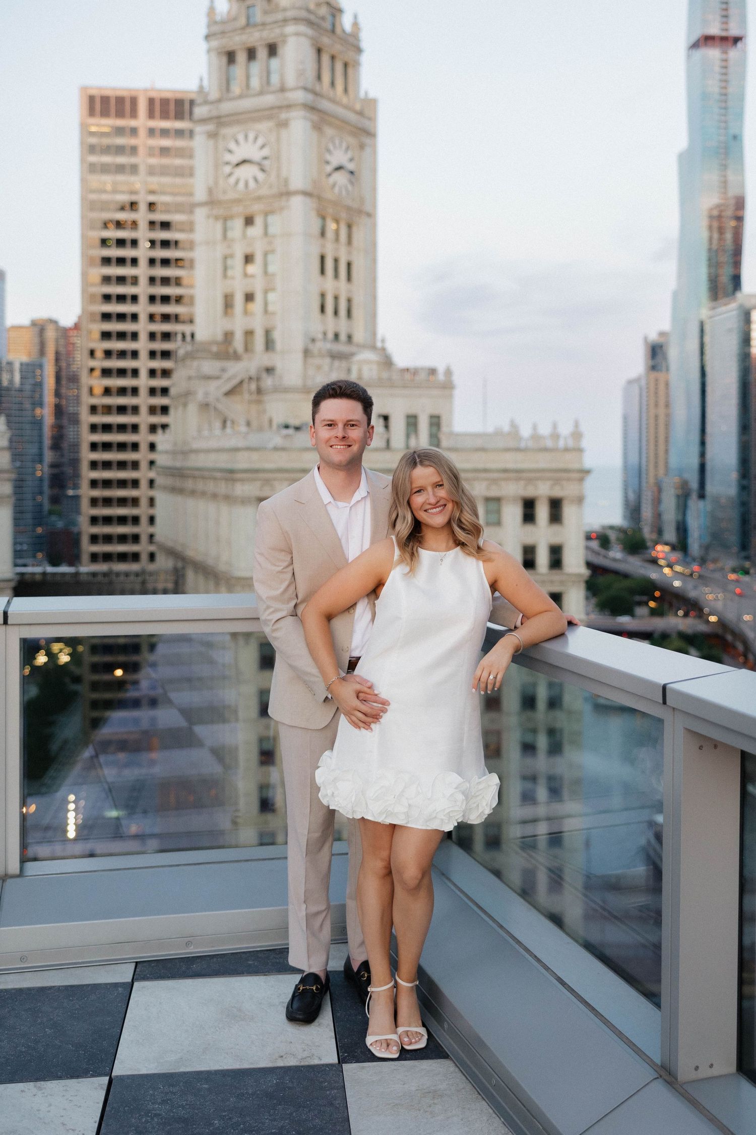 Couple posing on rooftop terrace with Chicago Wrigley Building and city skyline at golden hour.