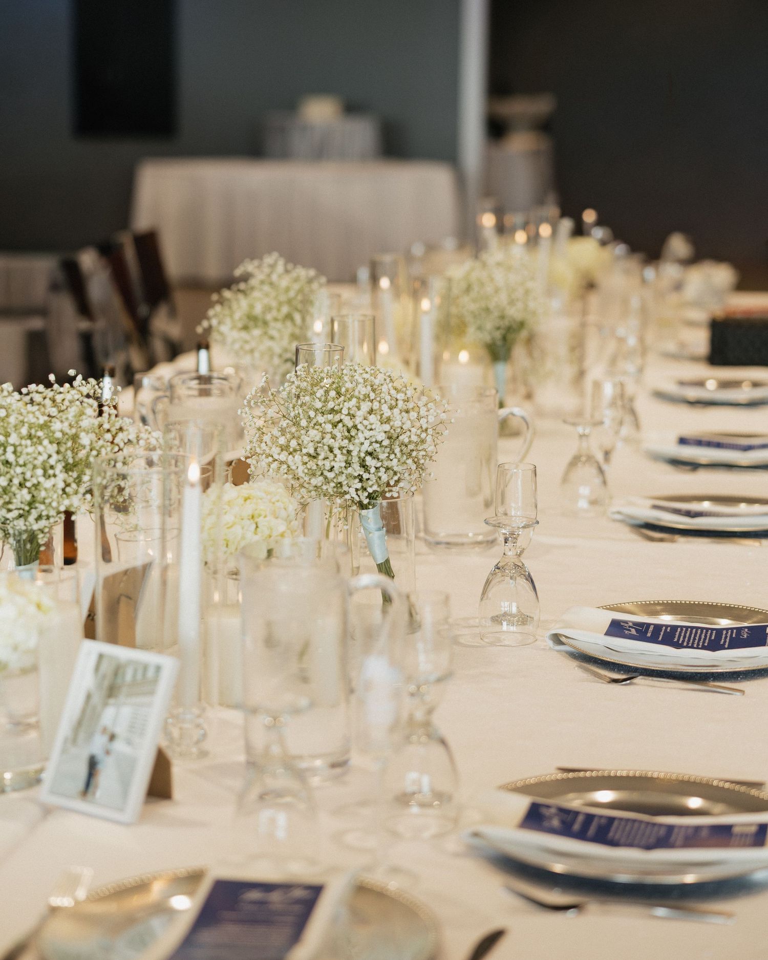 Elegant wedding reception table with baby's breath centerpieces, white candles, and navy blue place settings.