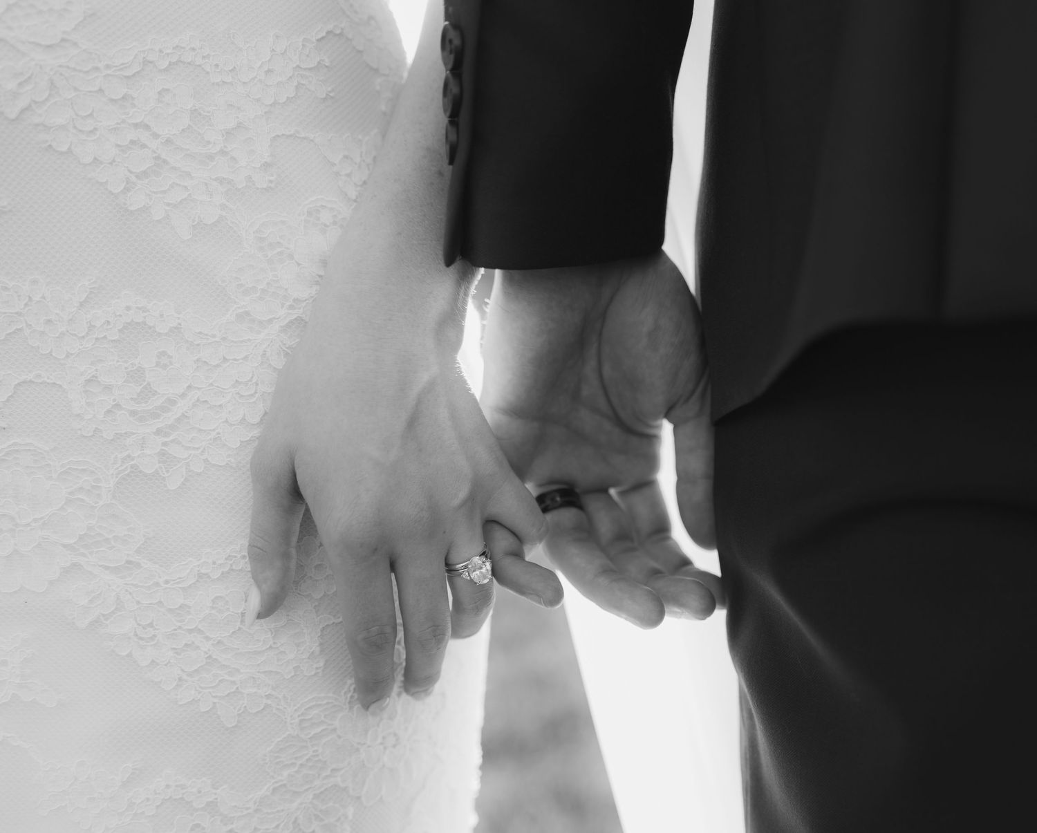 Black and white close-up of newlyweds holding hands.