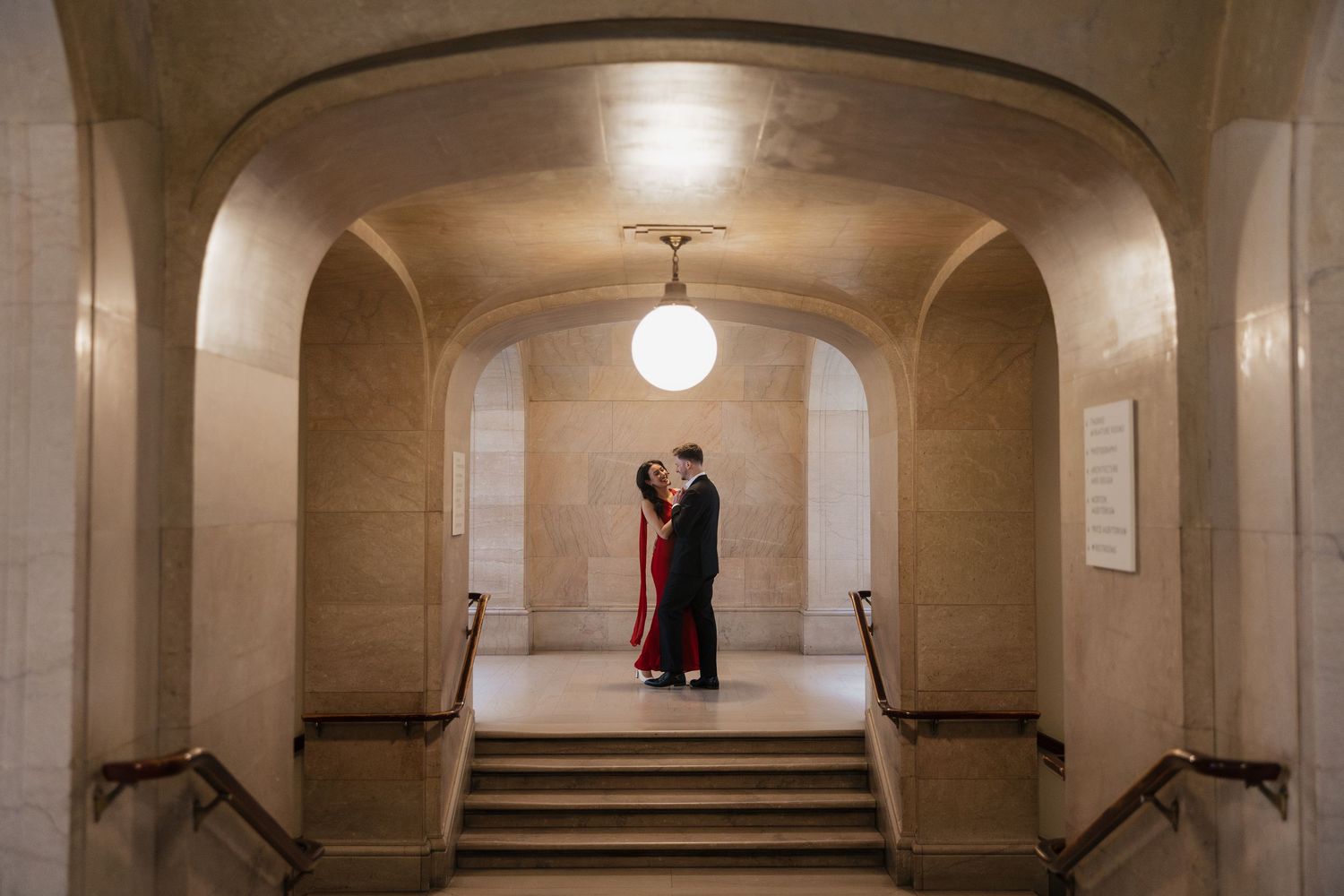 Curved stone archways and pendant lights create a symmetrical corridor in a historic building interior.