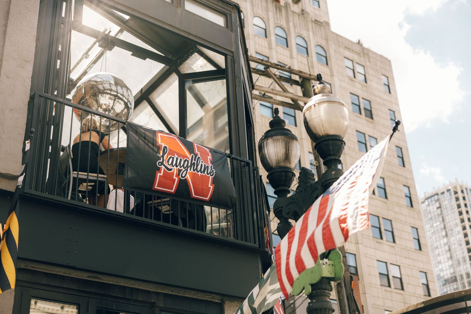 Outdoor restaurant patio with black metal awning structure and American flags mounted on brick building exterior.
