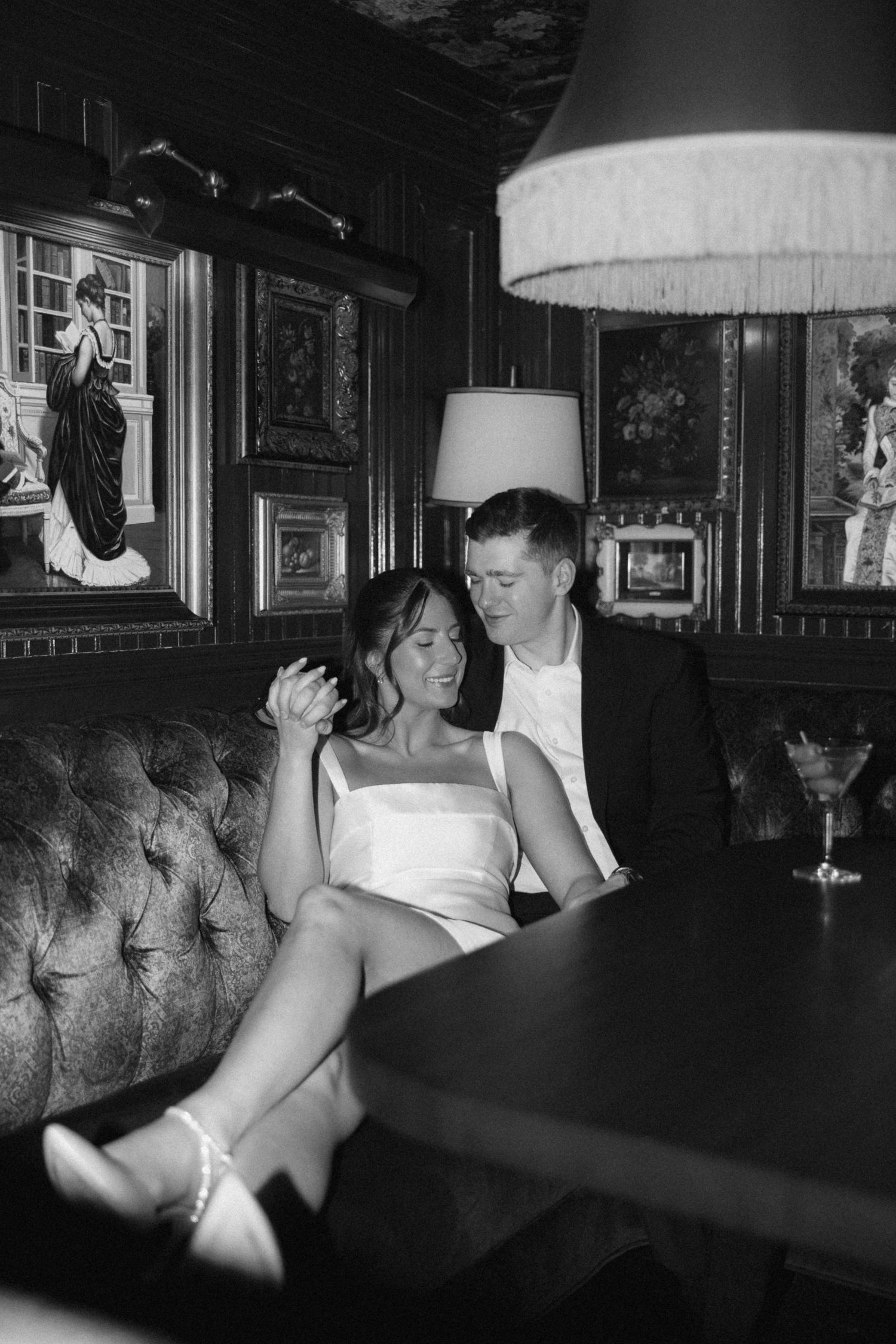 Monochrome interior shot of patrons at a bar counter with vintage decor and lighting fixtures.