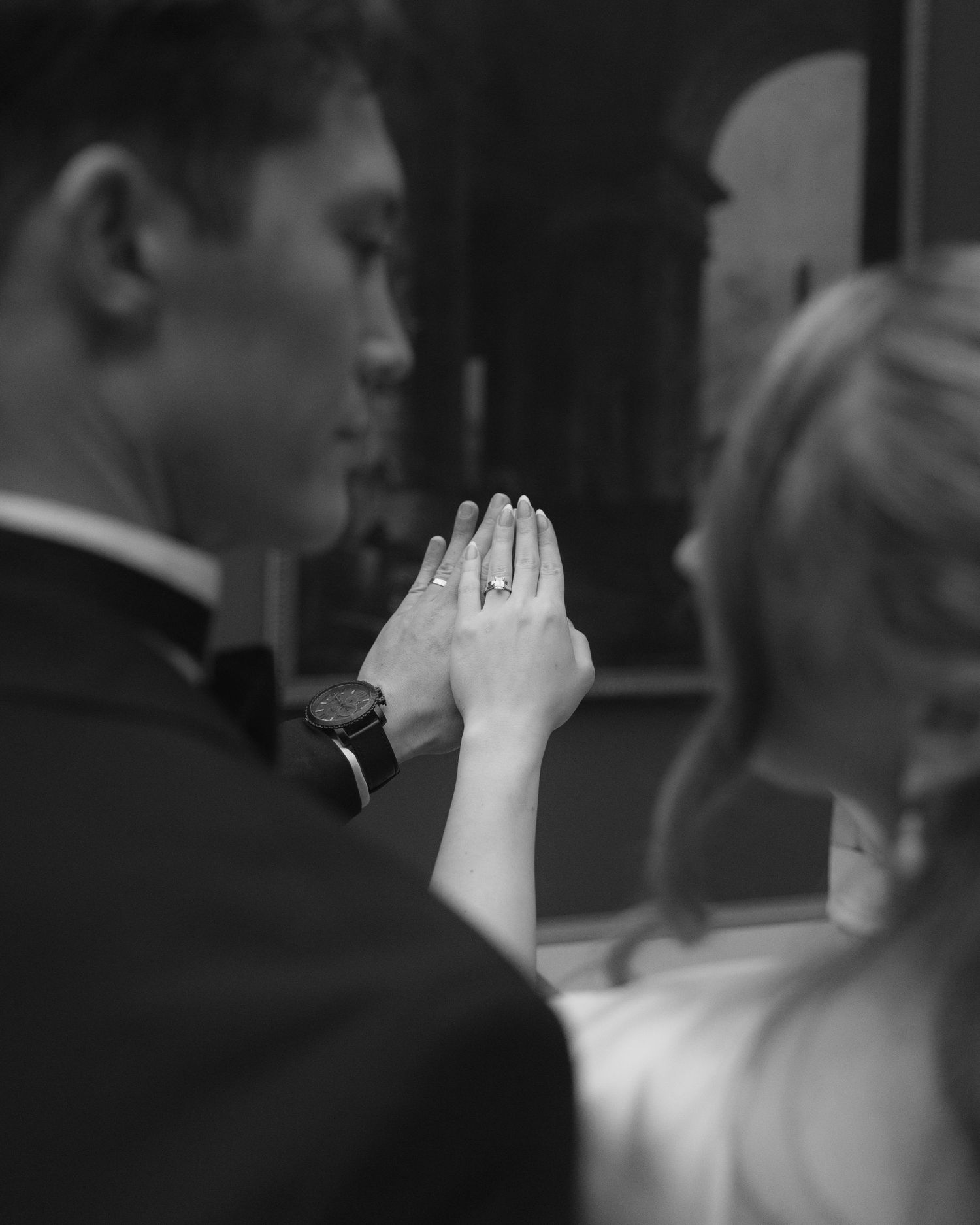 A black and white wedding photo showing hands with rings held together in an intimate moment.