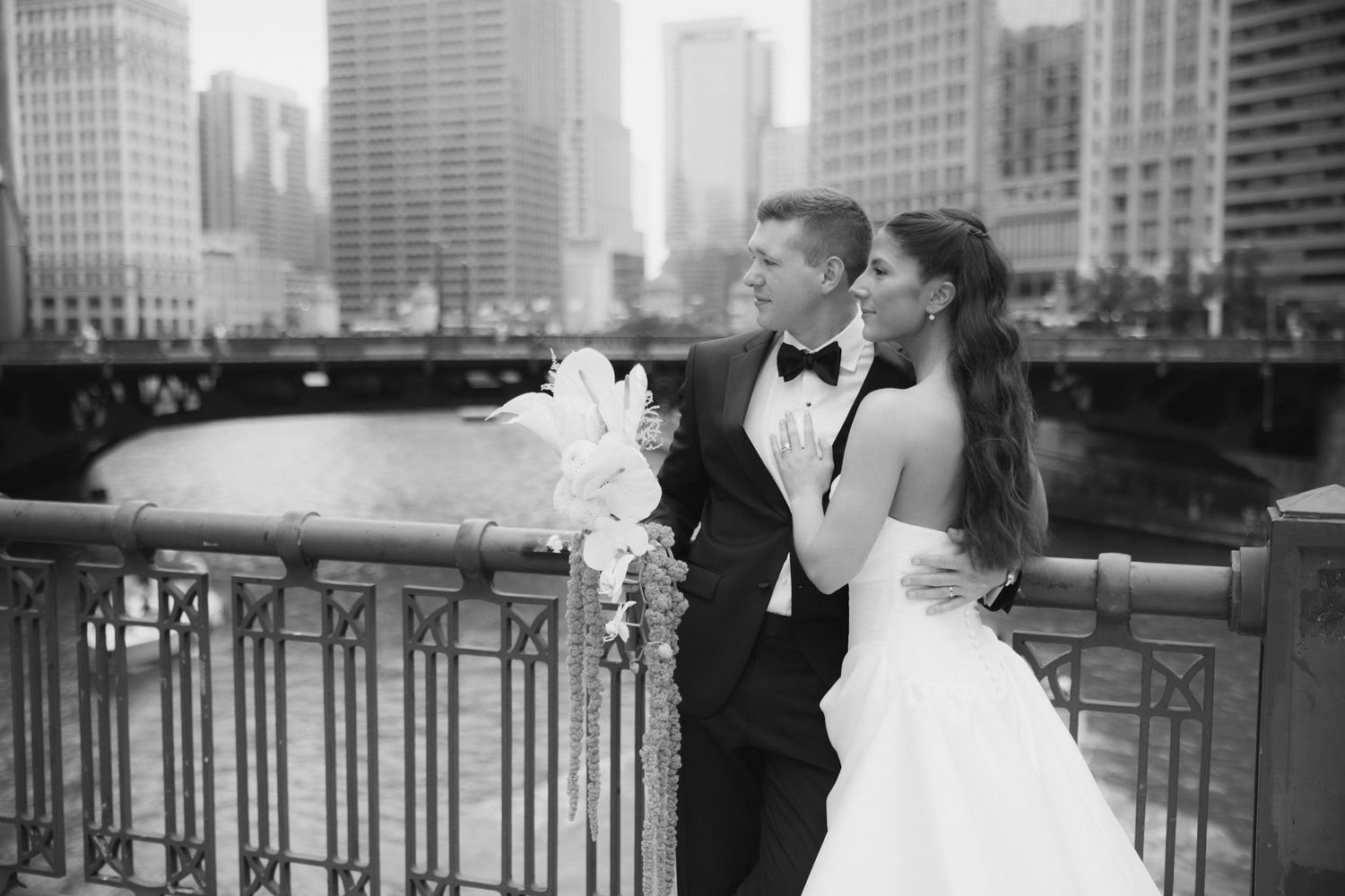 Black and white wedding photo of bride and groom embracing on a bridge with Chicago city skyline in the background.