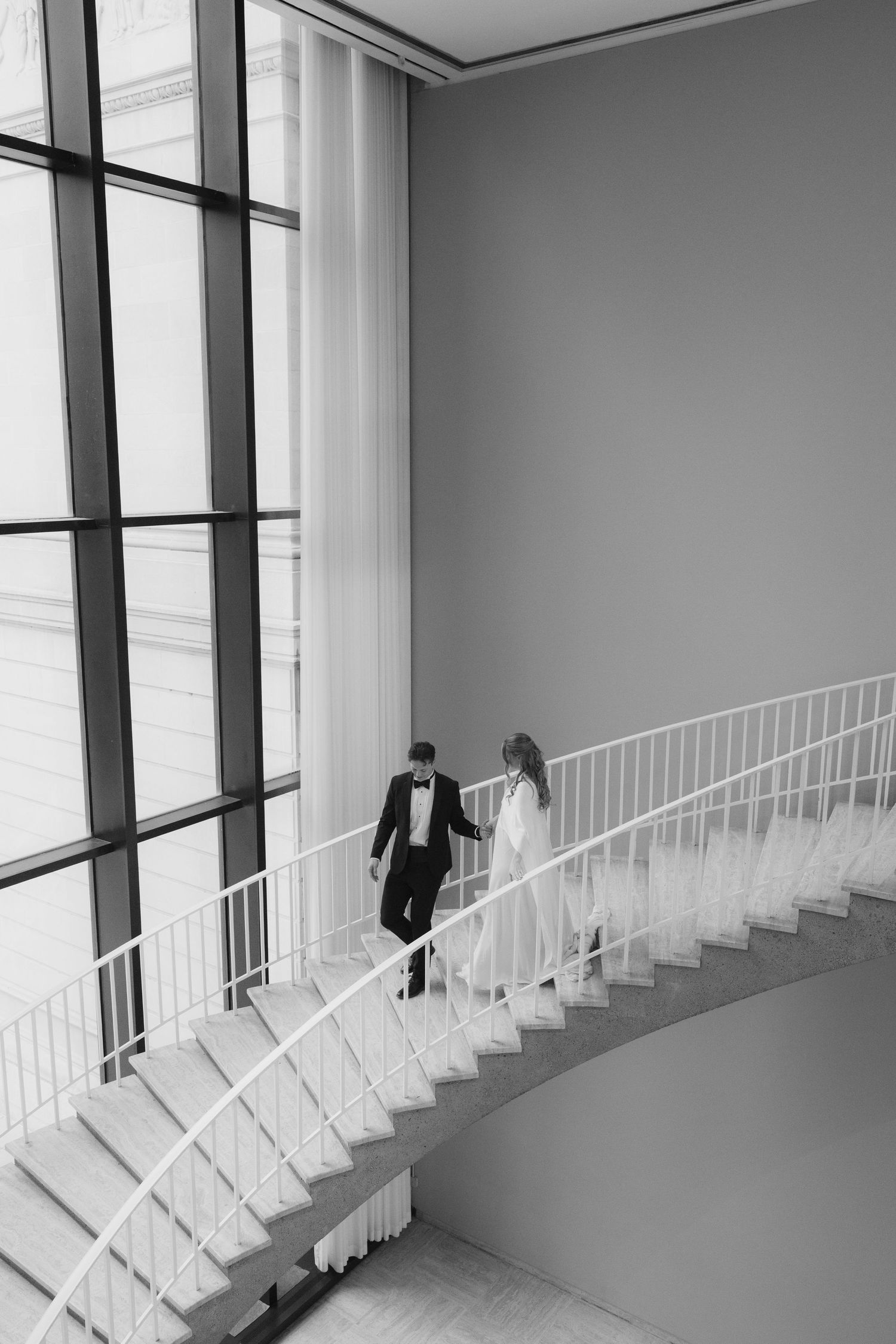 Black and white photo series showing a couple in formal wedding attire descending an elegant curved white staircase.