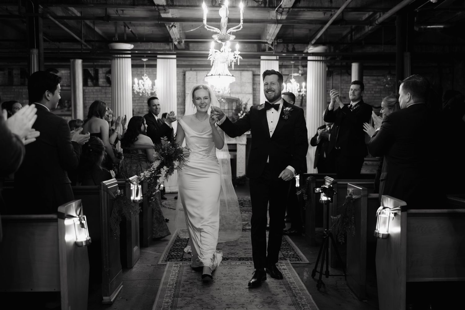 Black and white photo of people dancing and celebrating at what appears to be a wedding reception.