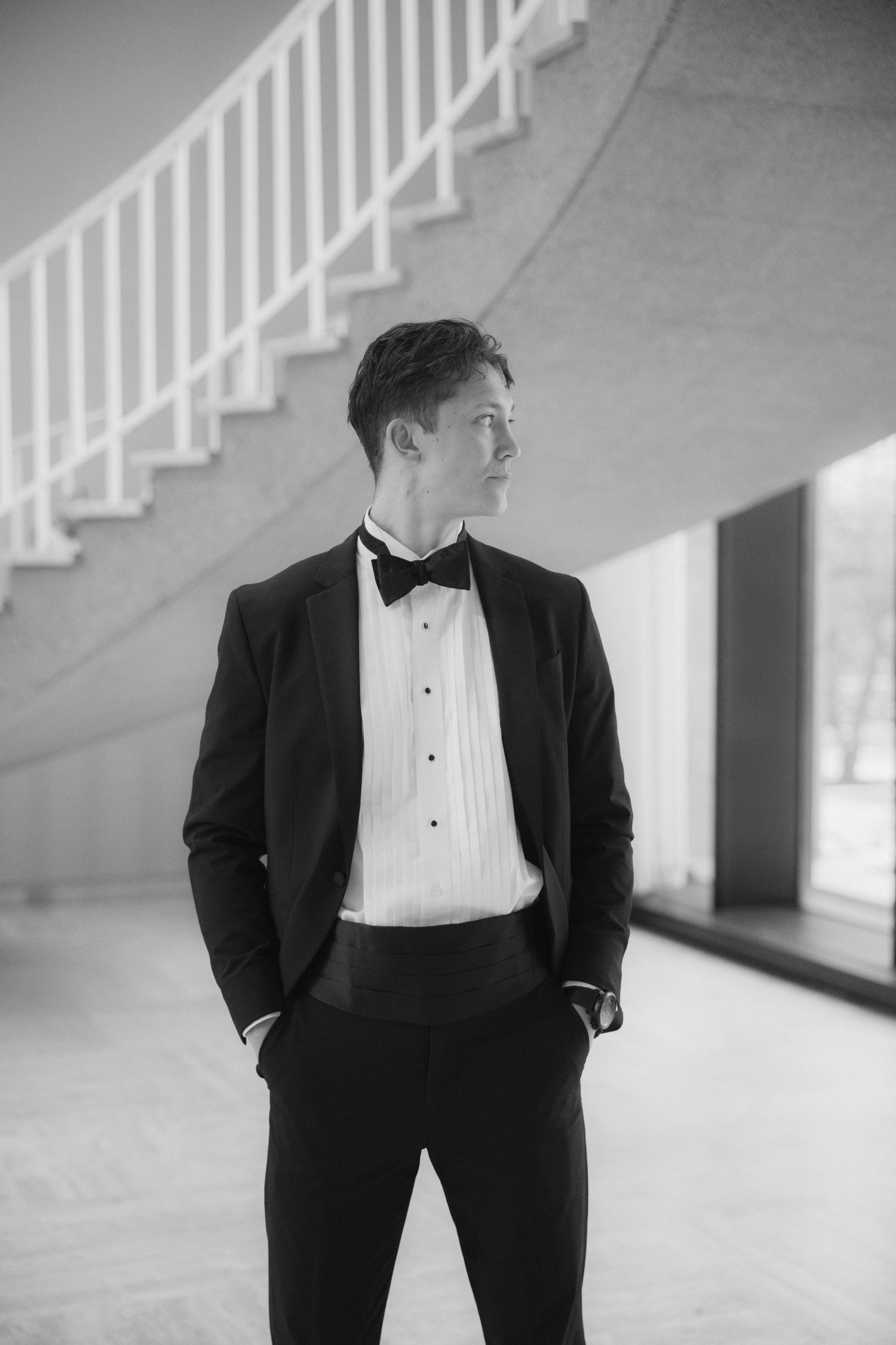 A series of black and white portraits showing a person in formal attire standing against a light wall with stairs.