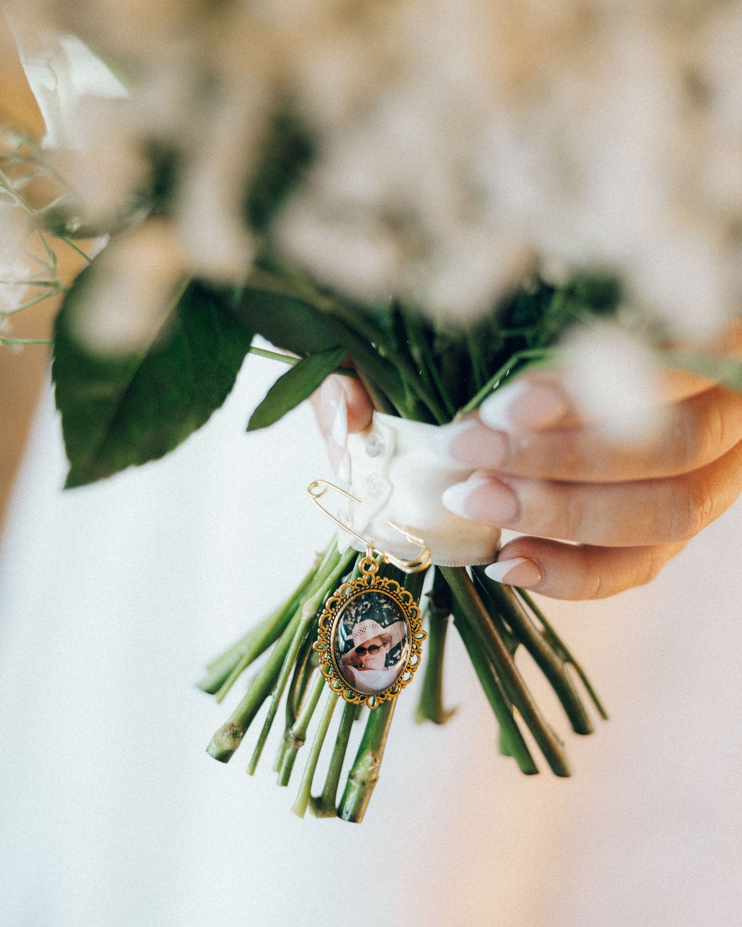 A close-up view of delicate white flowers with green stems being held by hands against a soft blurred background.