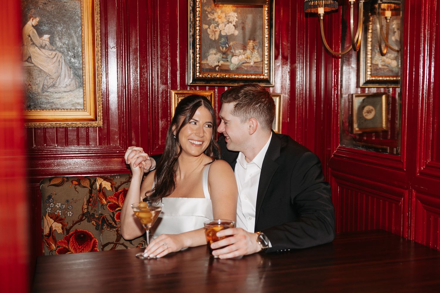 A couple shares an intimate moment in a luxurious red-walled room with ornate decor and vintage artwork.