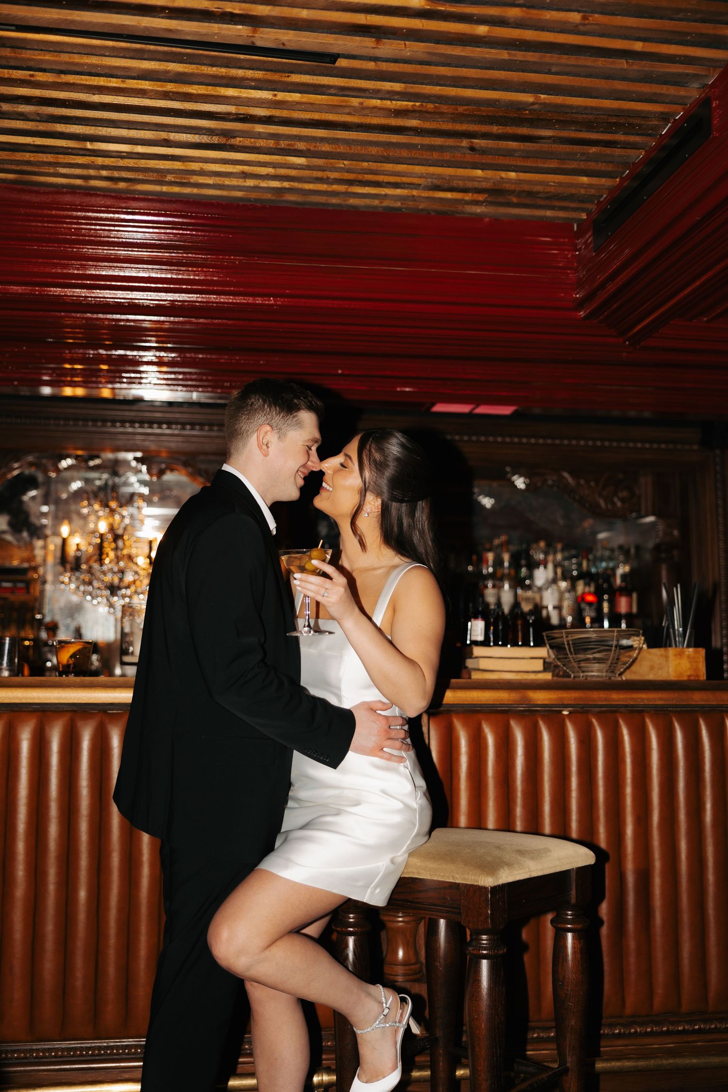 Romantic couple sharing an intimate moment at a dimly lit vintage bar with wood paneling and leather seating.